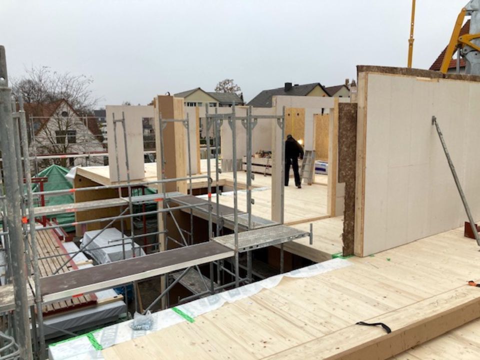 Baustelle: Holzwände und Gerüst. Eine Person arbeitet in einer teilweise fertiggestellten Struktur.