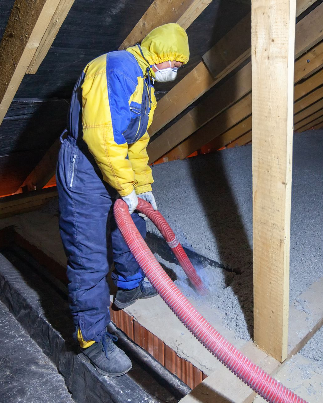 Un artisan en combinaison jaune et bleue réalise l'isolation de combles.