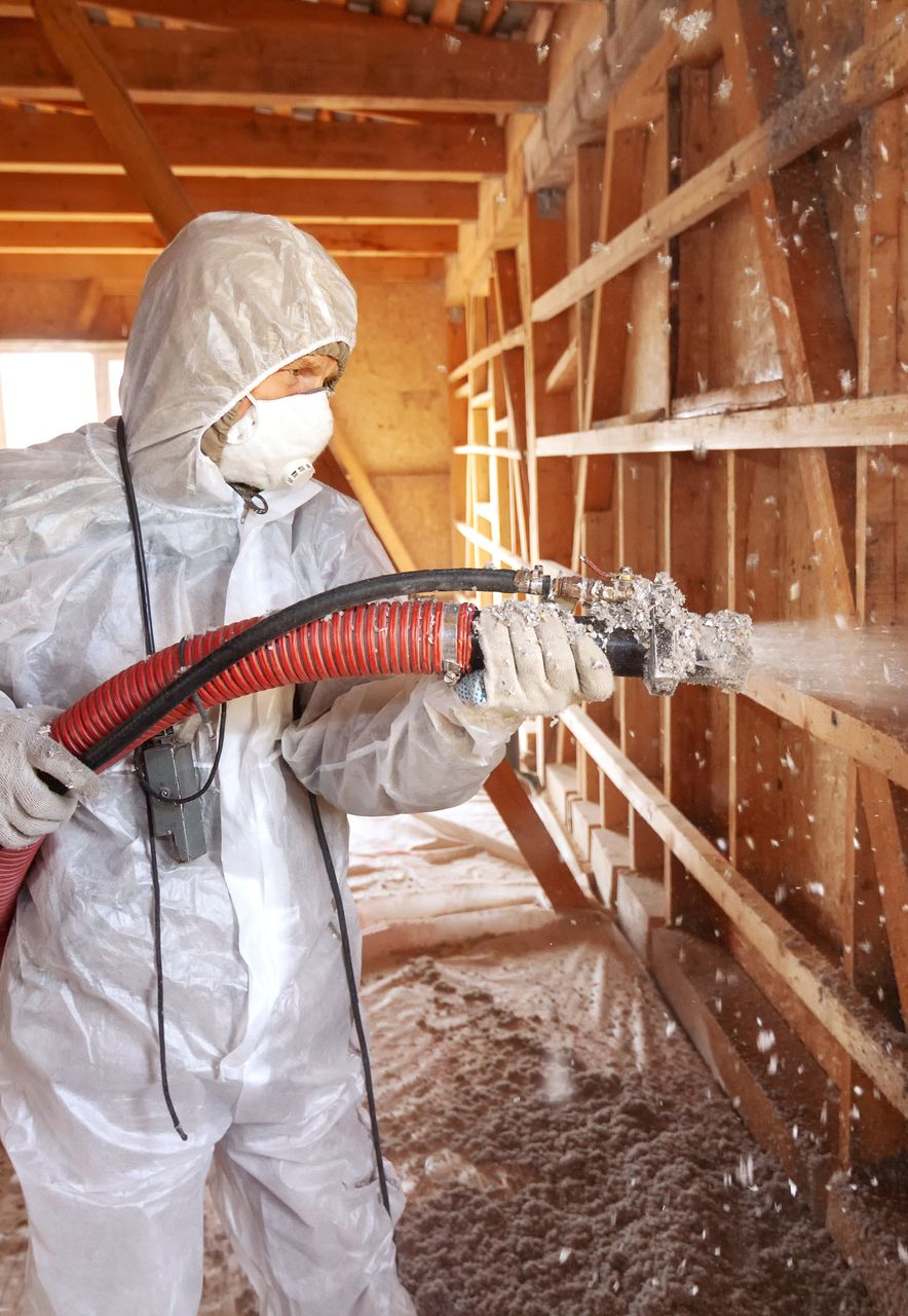 Un artisan en combinaison blanche réalise une isolation par soufflage.
