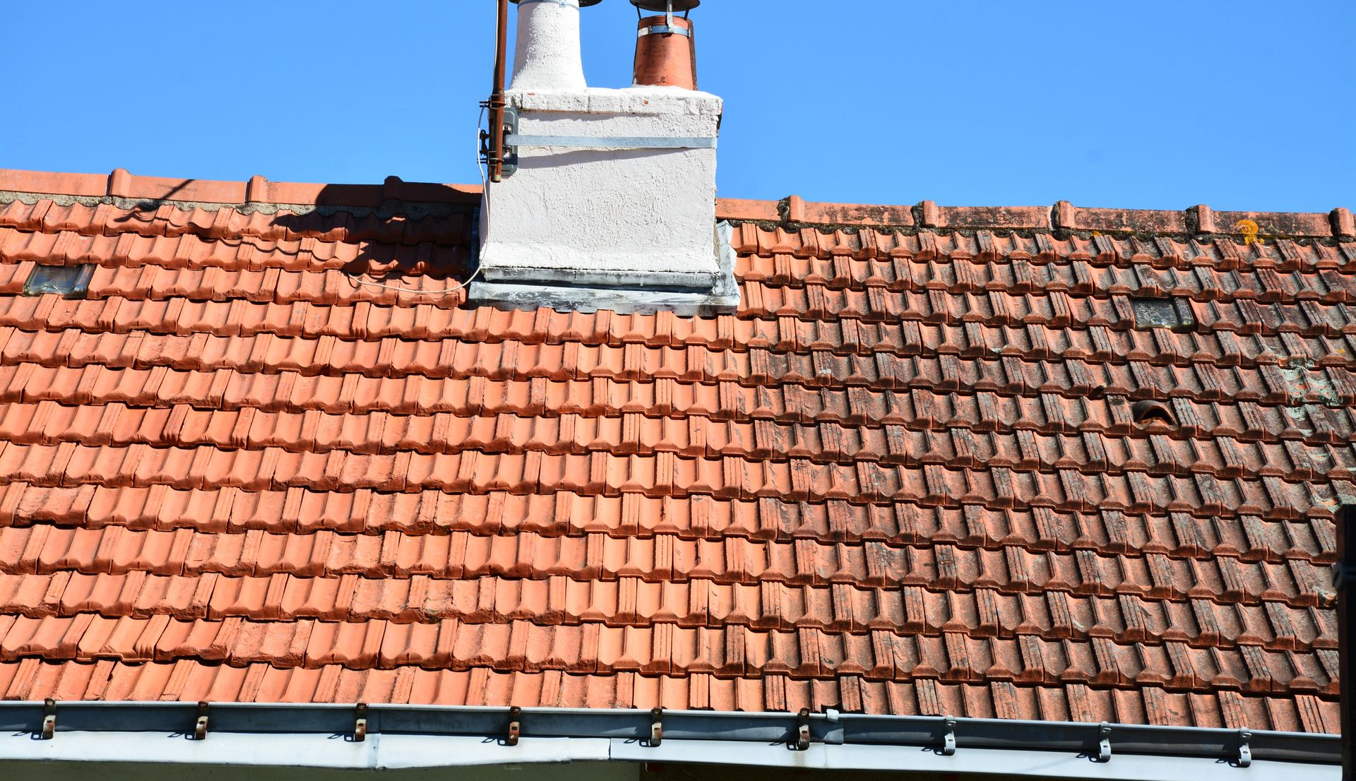 Toiture en tuiles rouges, à moitié nettoyée.