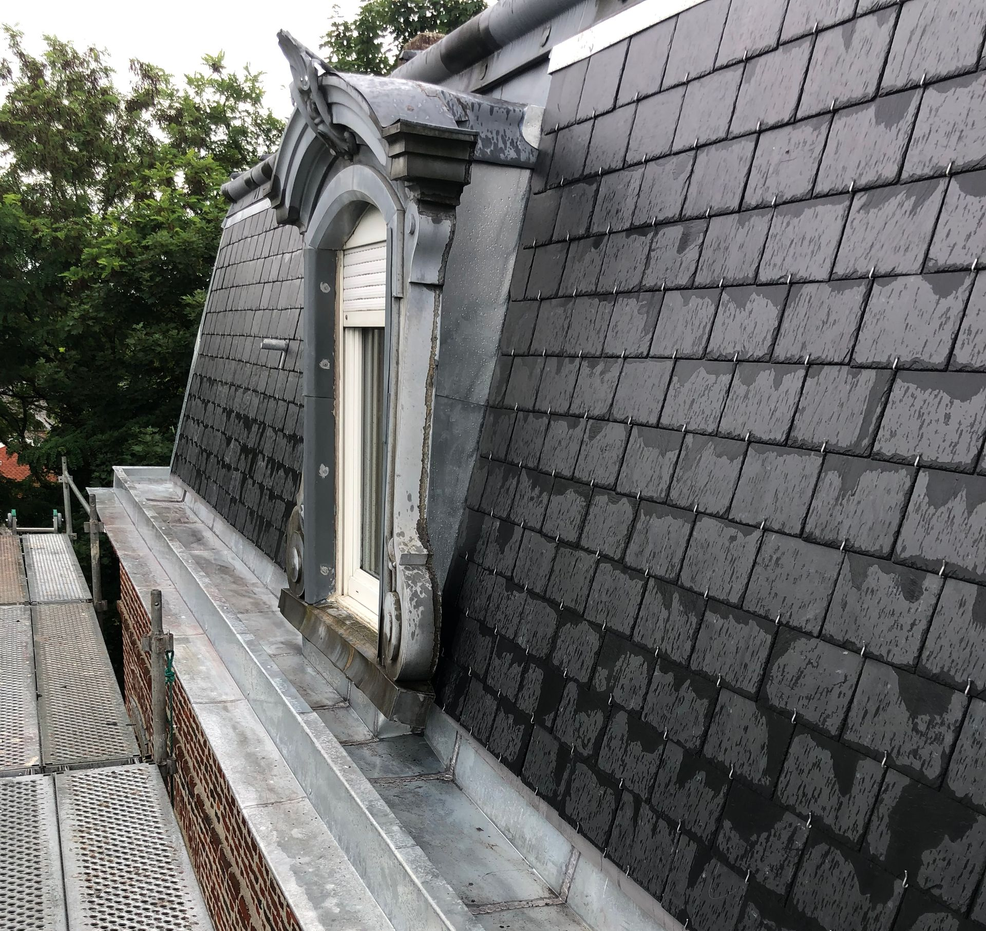 Toit en ardoise grise avec une lucarne, pluie et échafaudages.