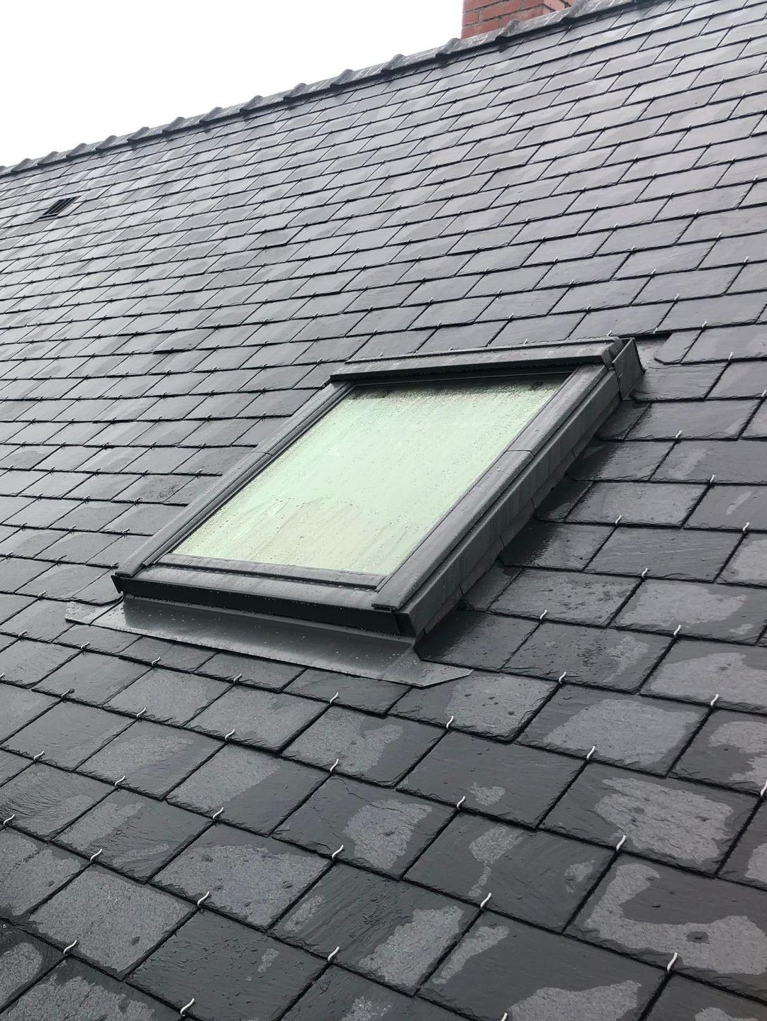 Une fenêtre de toit sur un toit de tuiles grises.