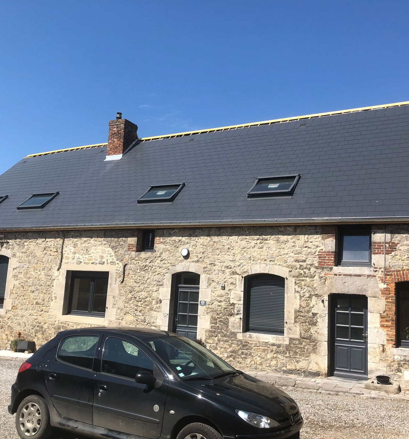 Toiture grise avec cheminée et trois fenêtres de toit.