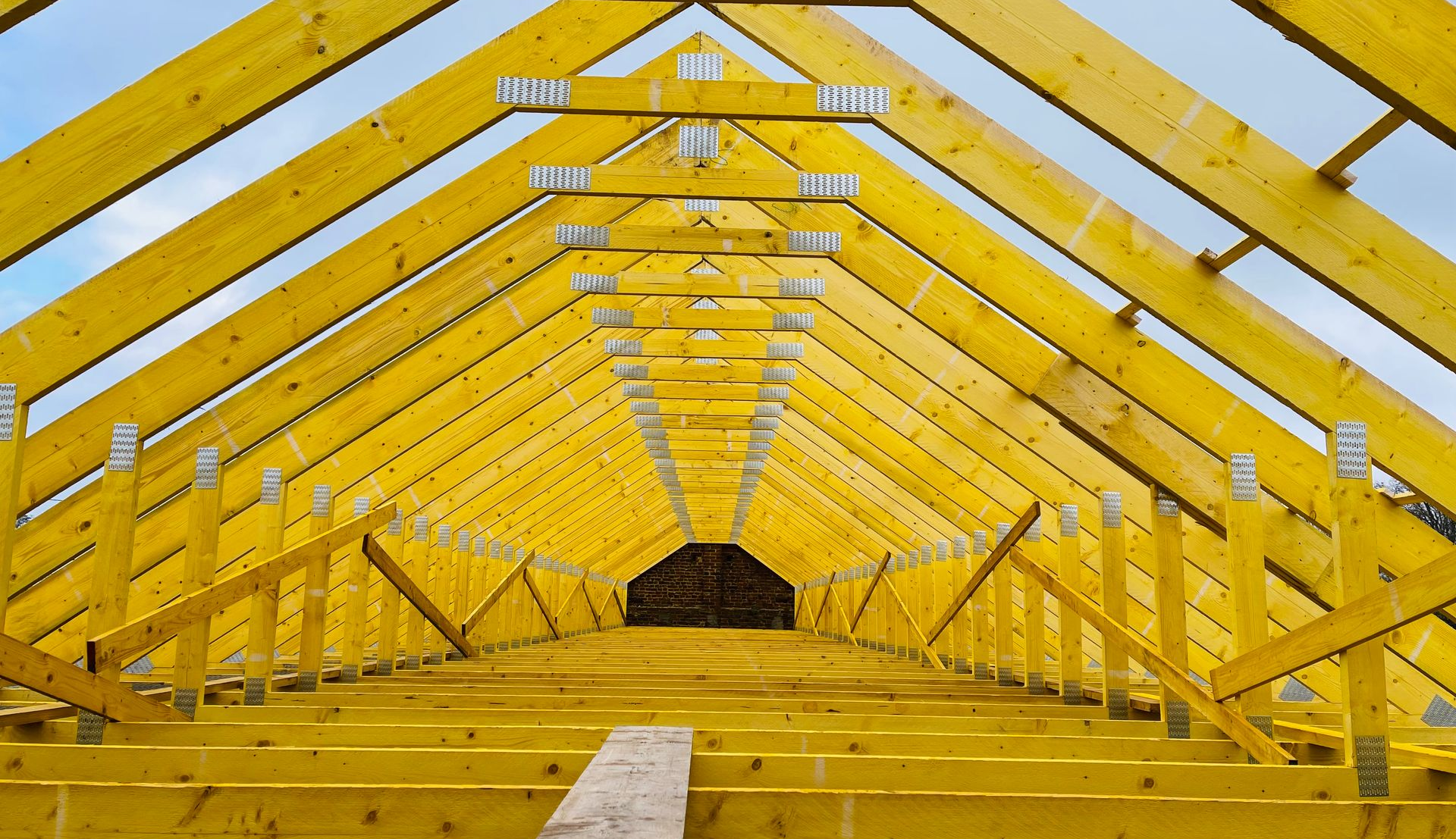 Charpente de toit en bois jaune sous un ciel lumineux.