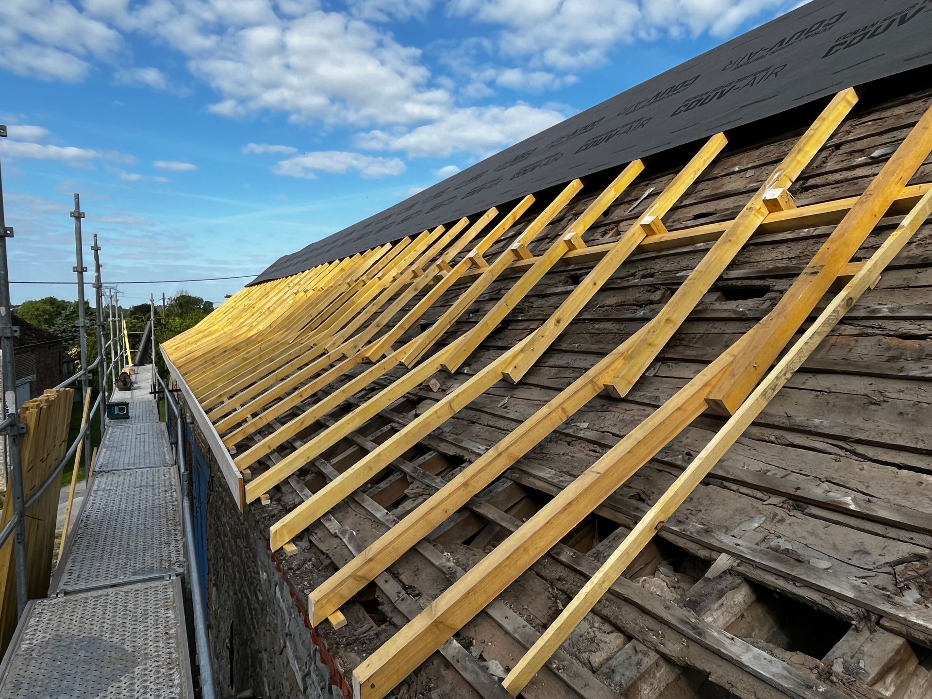 Toiture avec de nouveaux chevrons en bois installés sur une ancienne toiture abîmée par les intempéries.