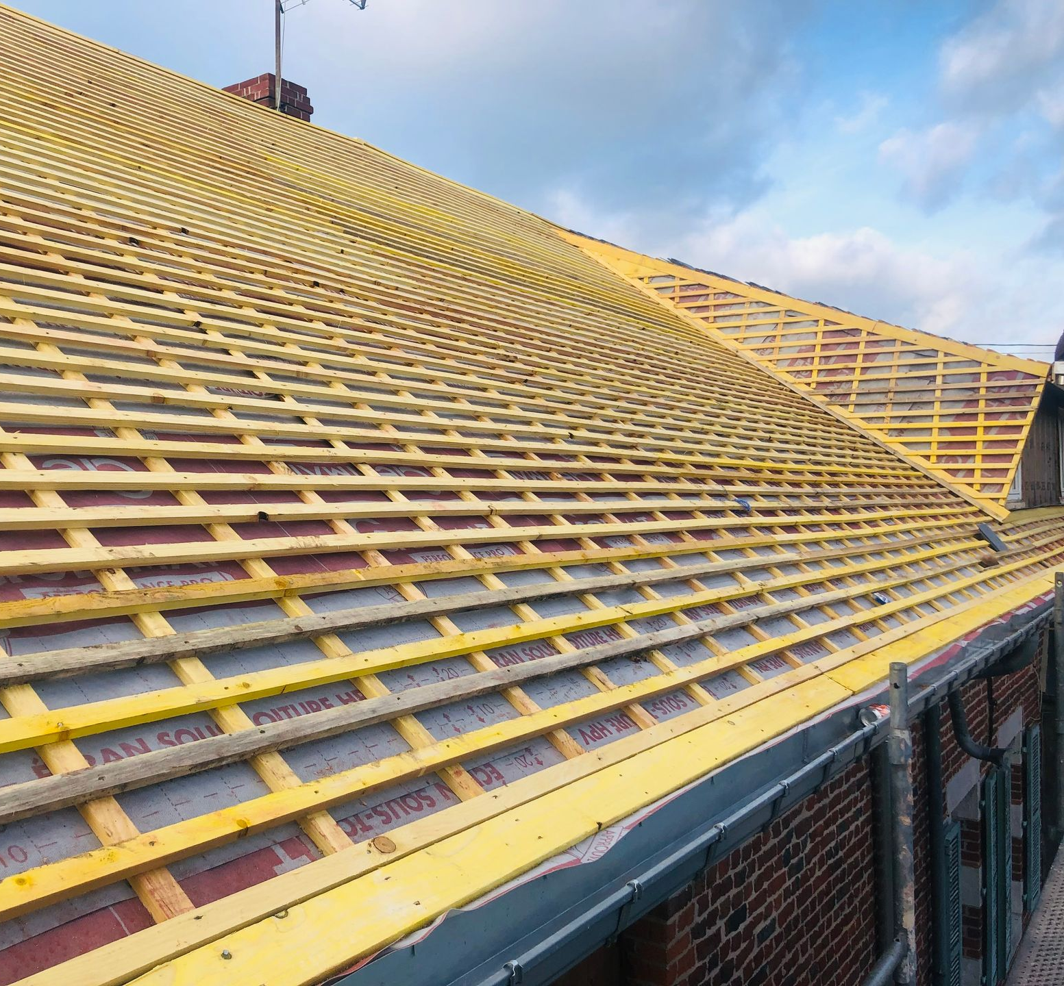 Toiture en construction ; poutres en bois et isolation visibles. Ciel bleu en arrière-plan.