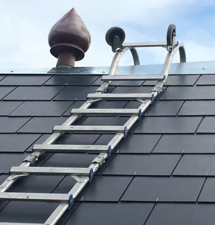 Échelle à roulettes sur un toit de tuiles sombres, près d'une cheminée.