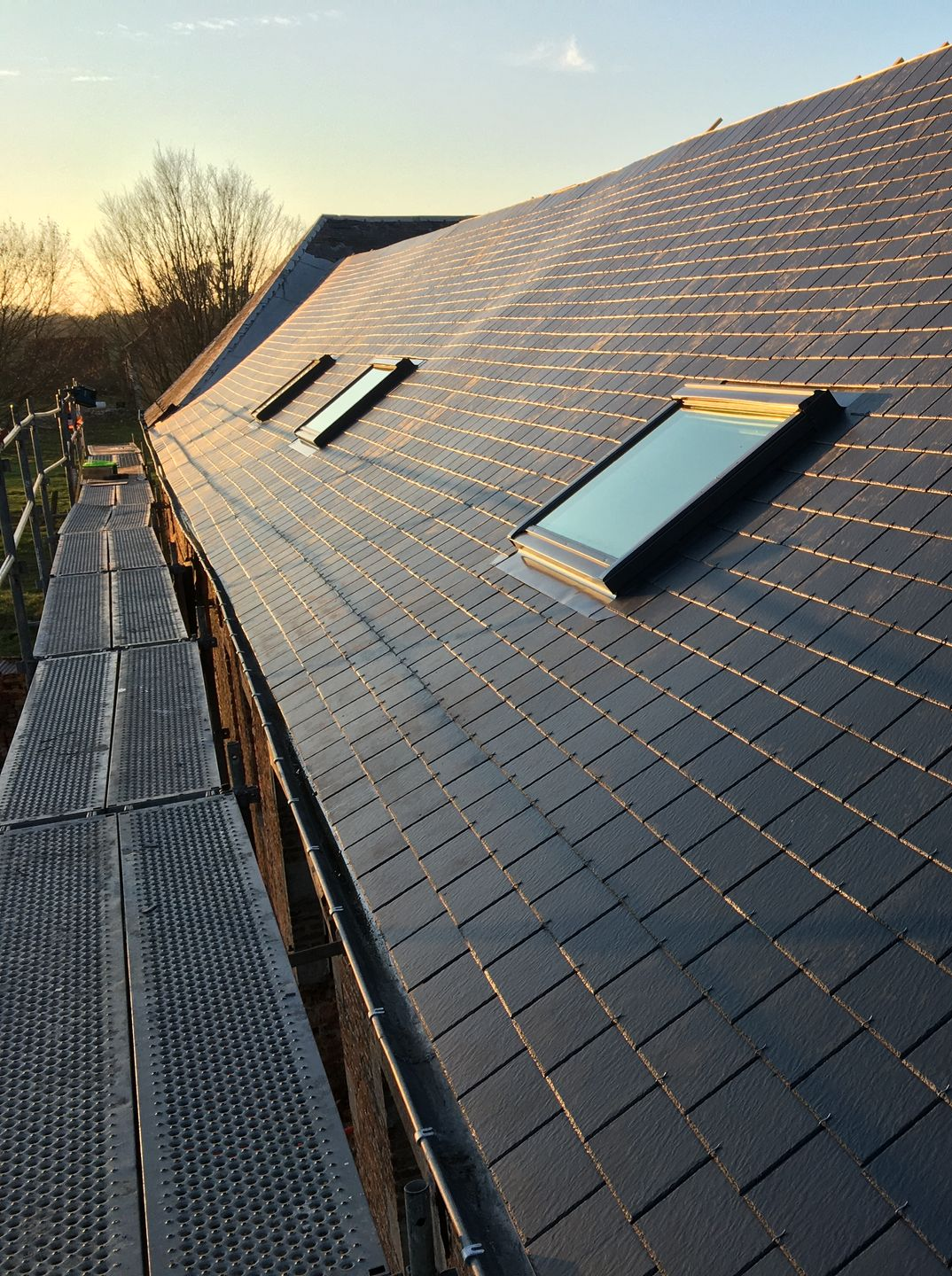 Trois fenêtres de toit sur une toiture grise.