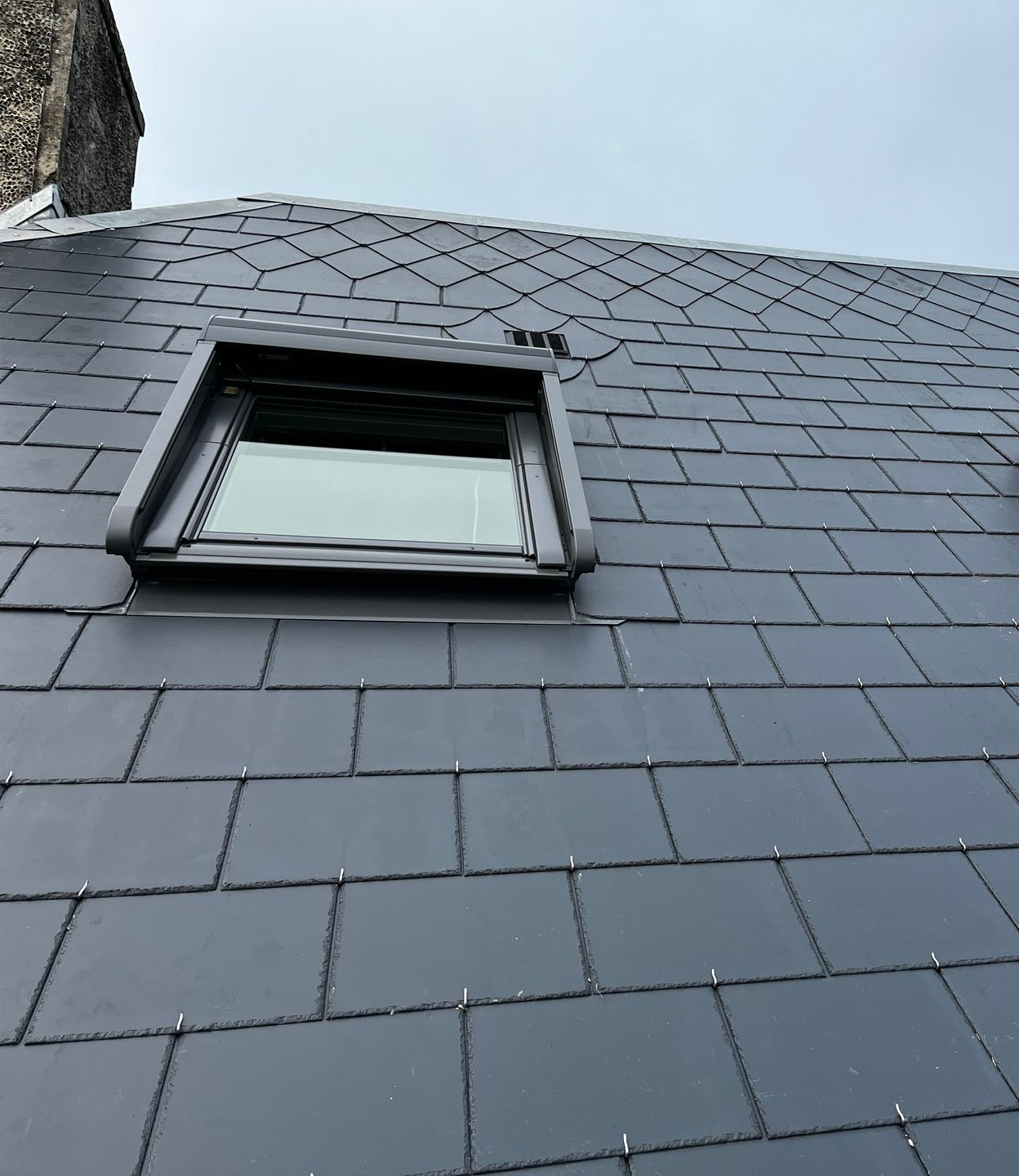 Une fenêtre de toit Velux sur une toiture en ardoise avec cheminée.