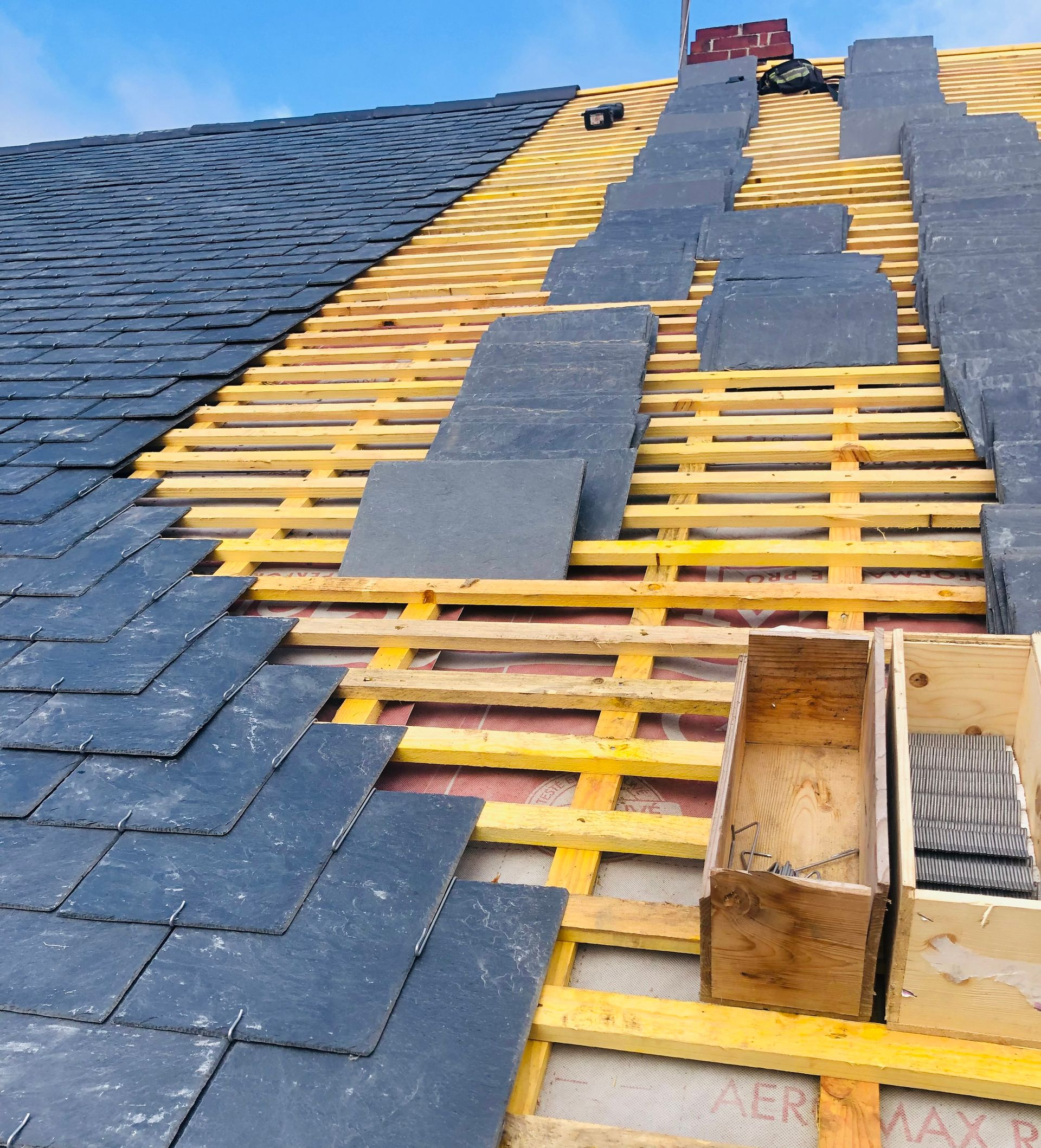 Une toiture en cours de rénovation : tuiles en ardoise posées sur une charpente neuve.