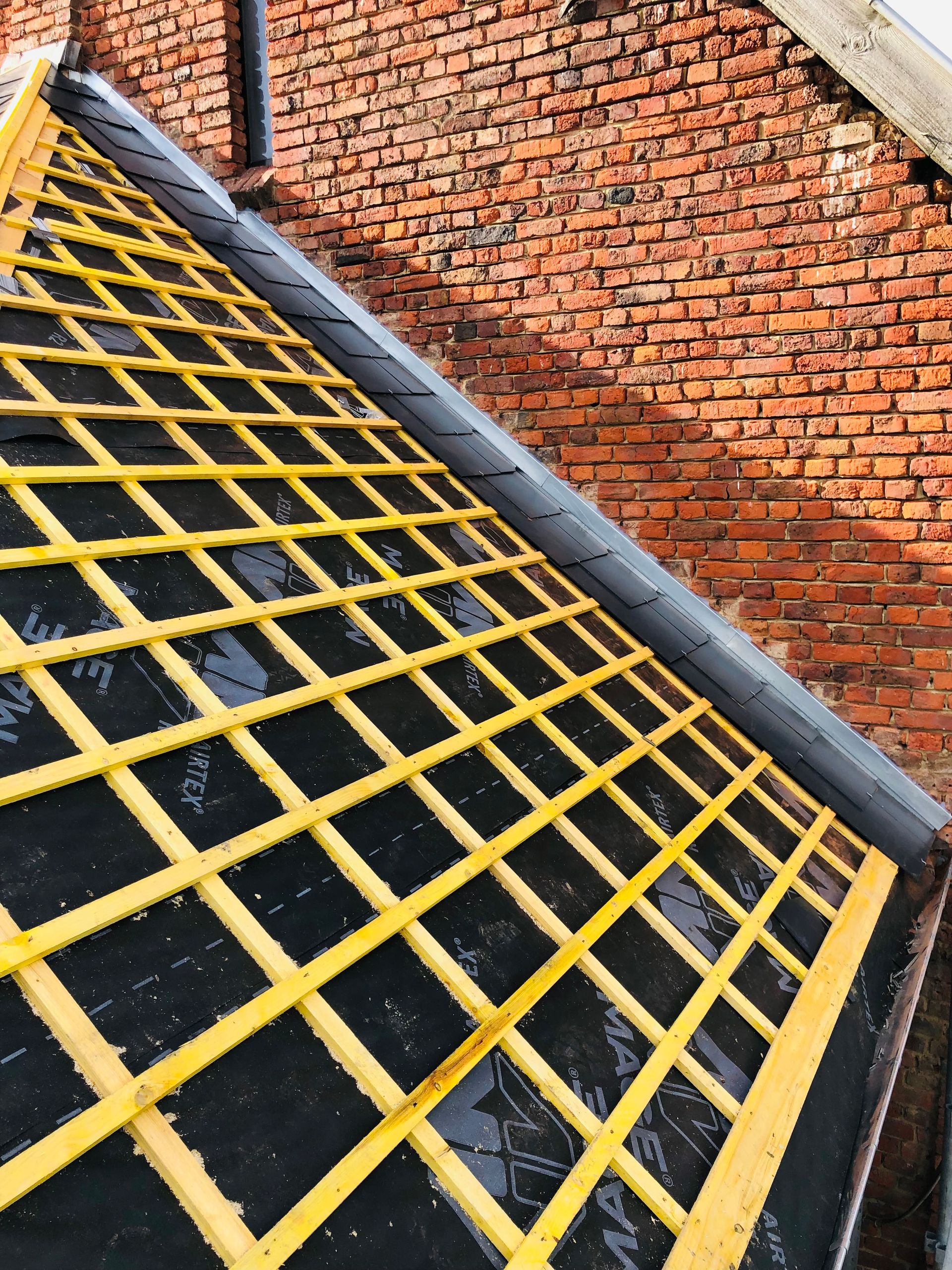 Treillis jaune sur fond sombre, devant un mur de briques.