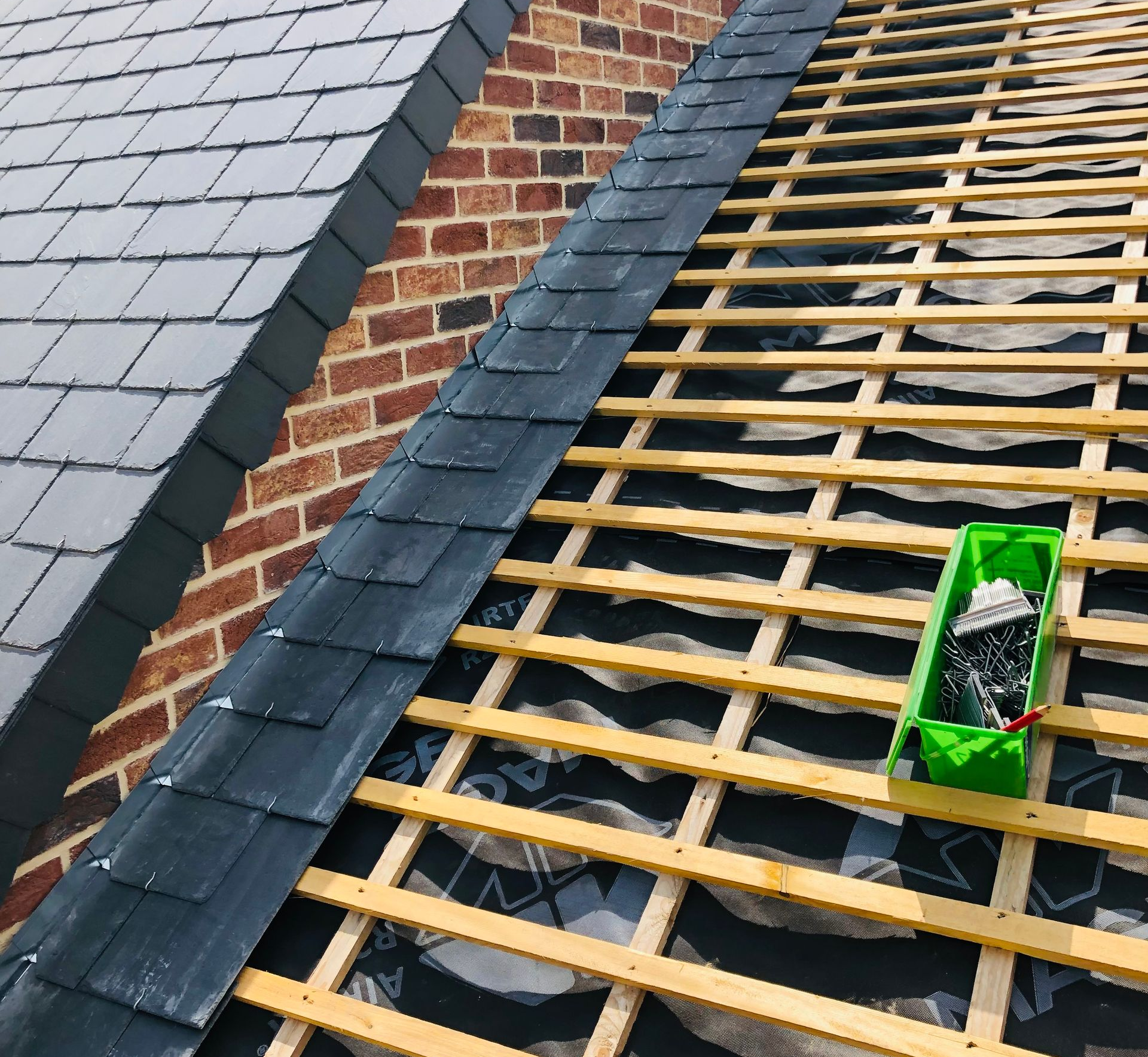 Construction de la toiture : pose d’ardoises à côté de chevrons en bois apparents, cheminée en briques.
