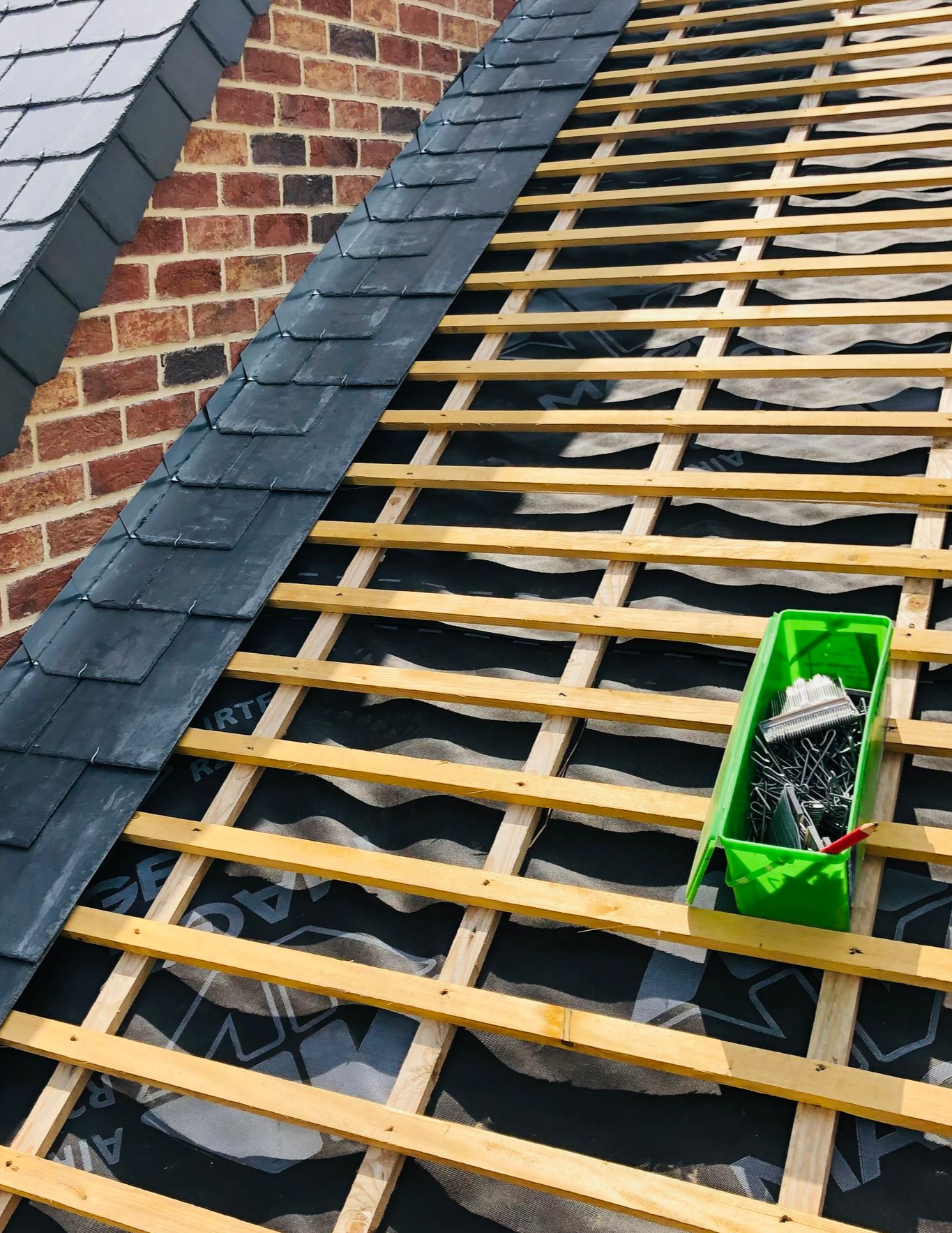 Maison partiellement couverte, bardeaux d'ardoise noire, charpente apparente, boîte à outils verte sur une bâche.