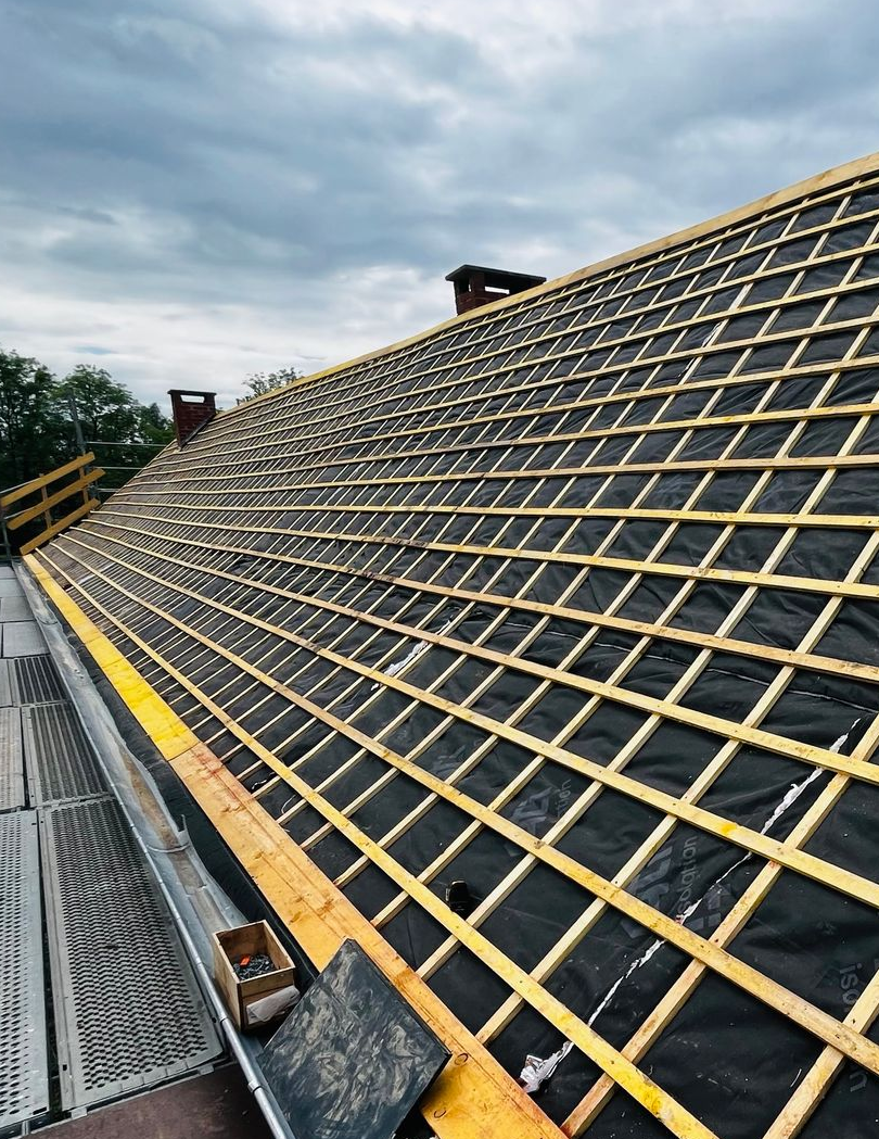 Toiture en construction avec poutres en bois et sous-couche noire.