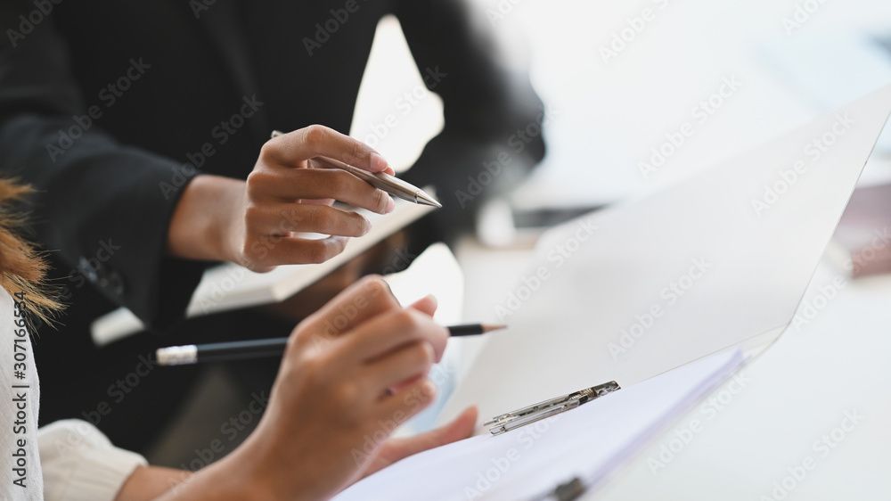 Zwei Personen in Geschäftskleidung prüfen Dokumente, eine von ihnen zeigt mit einem Stift darauf.