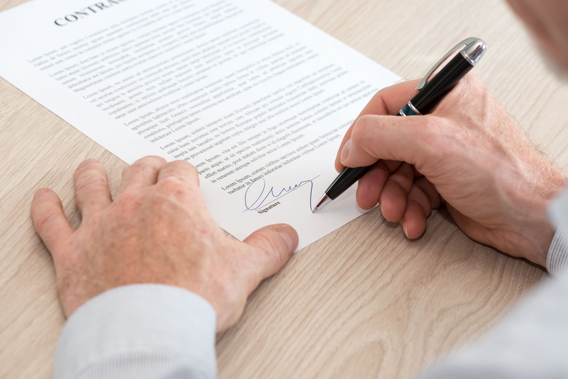 Des mains signent un contrat sur un bureau avec un stylo noir.