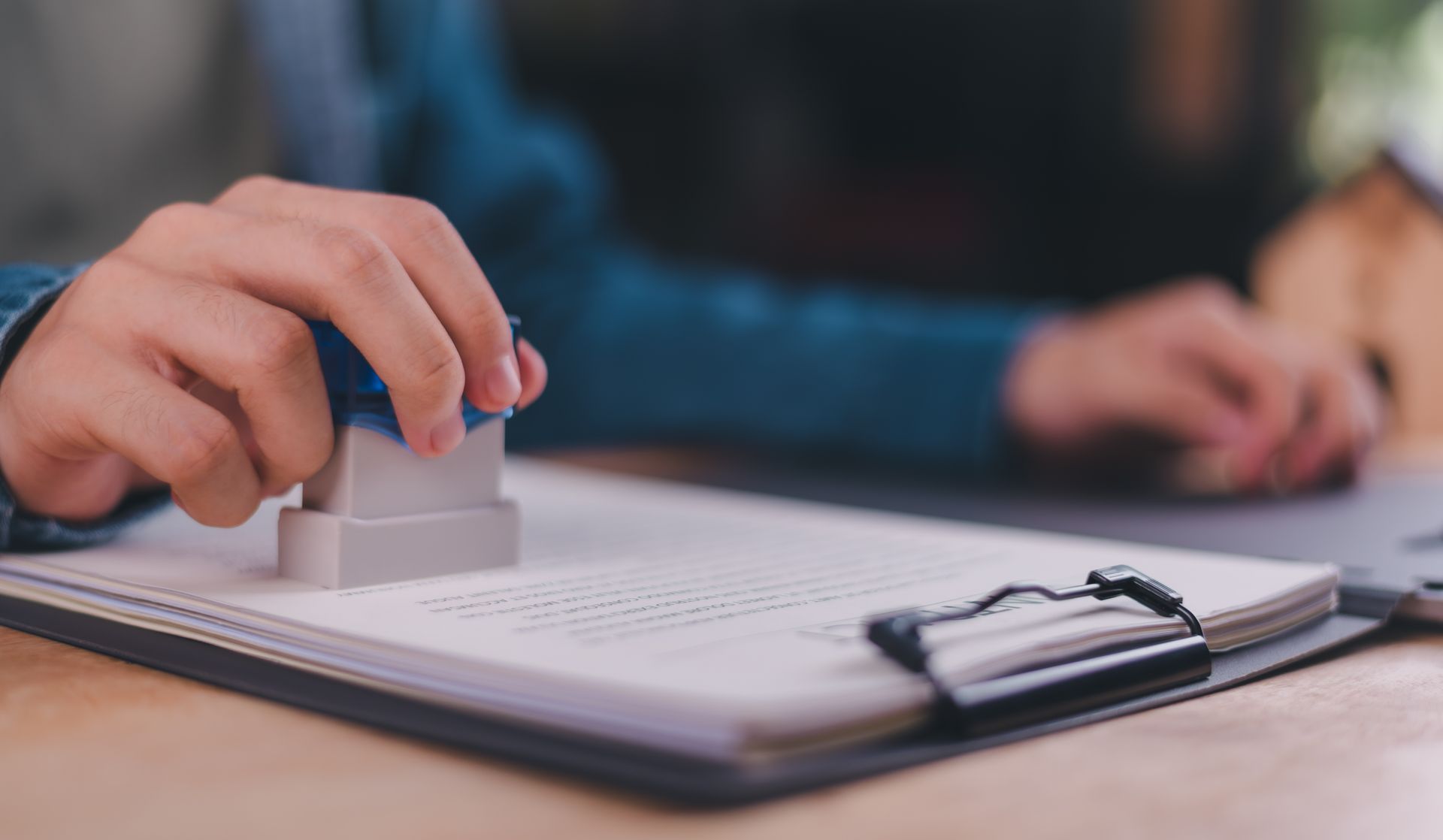 Une personne appose un tampon manuel sur un document posé sur un bureau.
