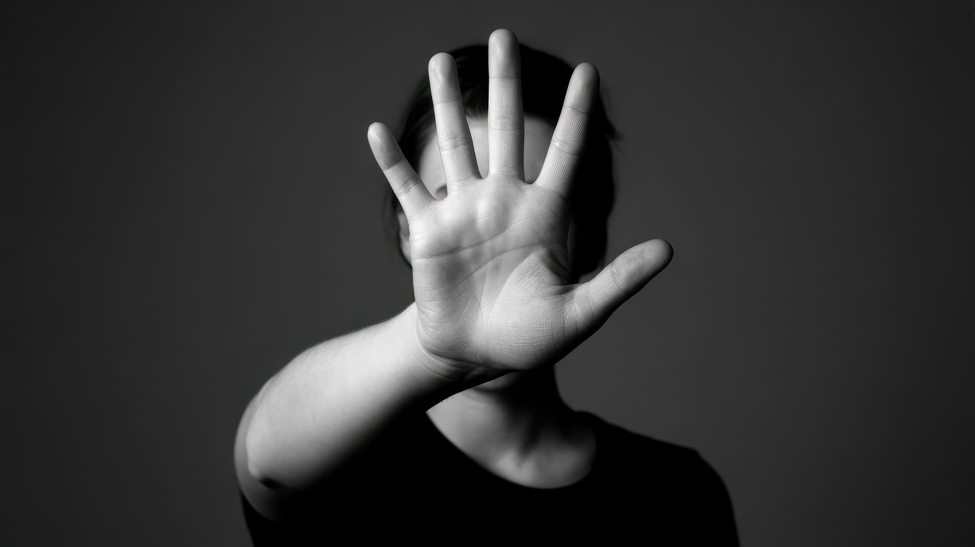 Personne la main levée cachant son visage sur fond sombre