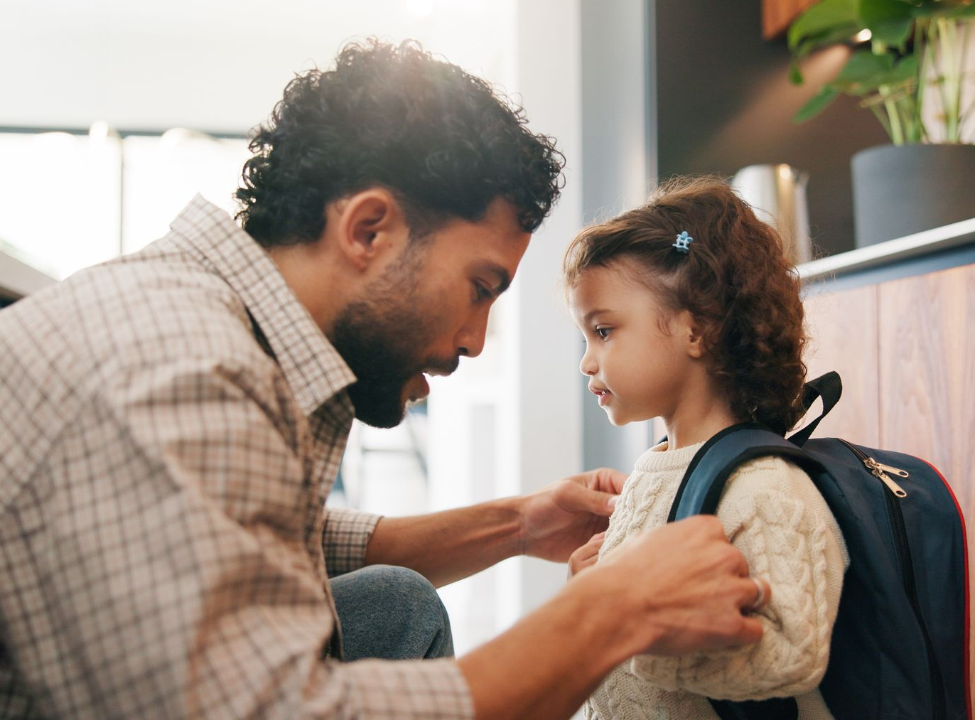 Un parent aide son enfant à ajuster son sac à dos avant l'école.