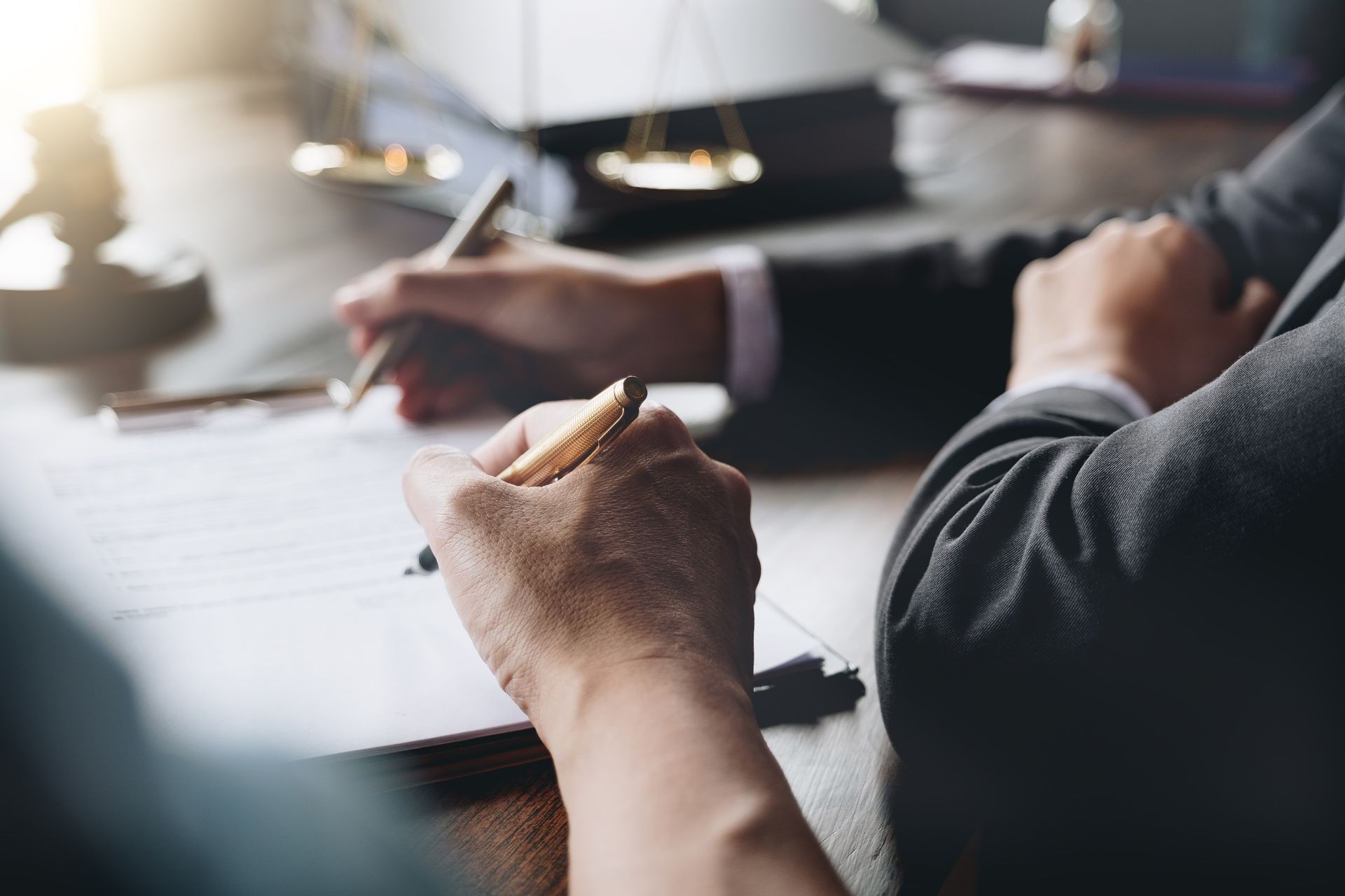 Une personne prend des notes à un bureau pendant une réunion, avec une balance de la Justice floue en arrière-plan.