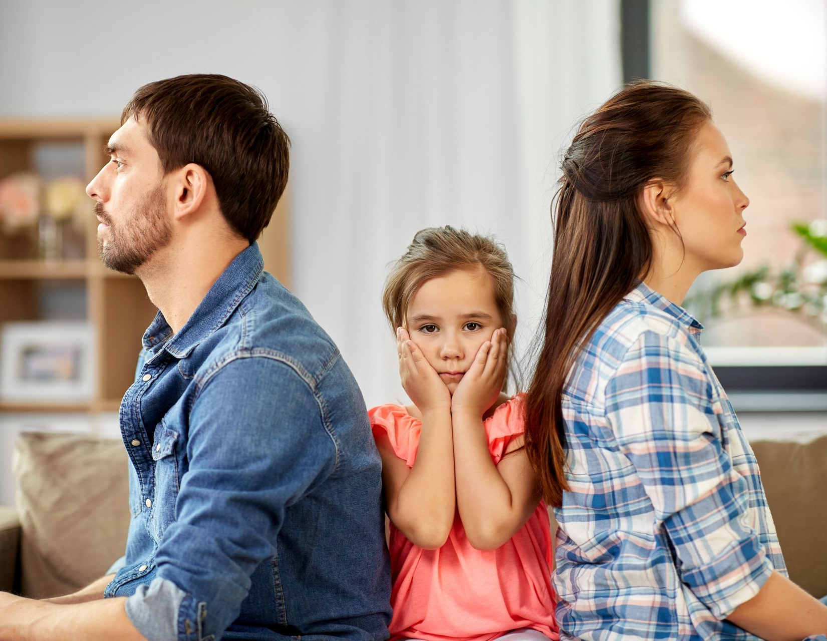 Une famille assise à distance les unes des autres sur un canapé, un enfant entre eux, les mains sur les oreilles.
