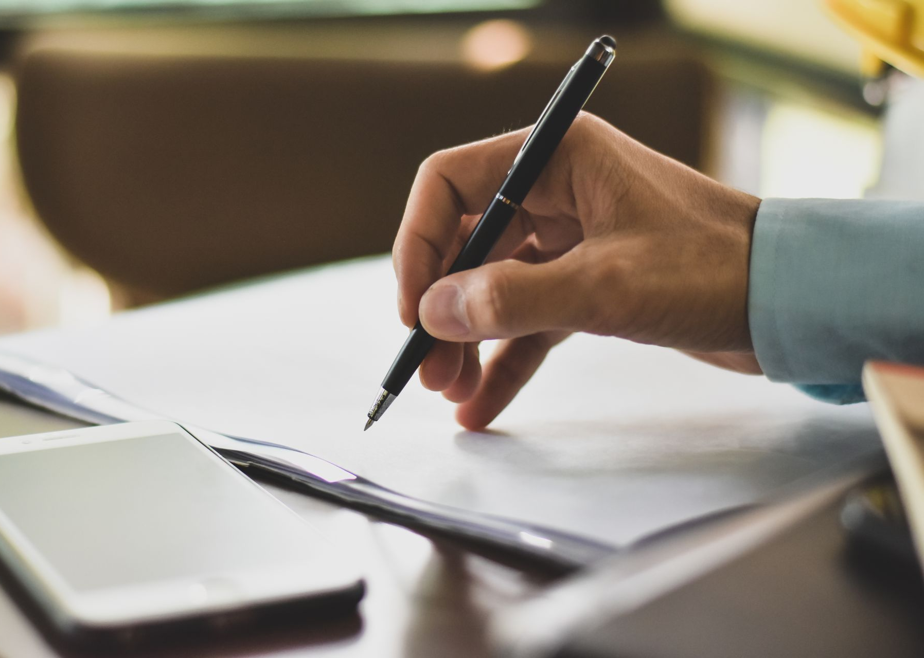 Écriture manuscrite au stylo noir sur une feuille de papier à côté d'un ordinateur portable posé sur un bureau.