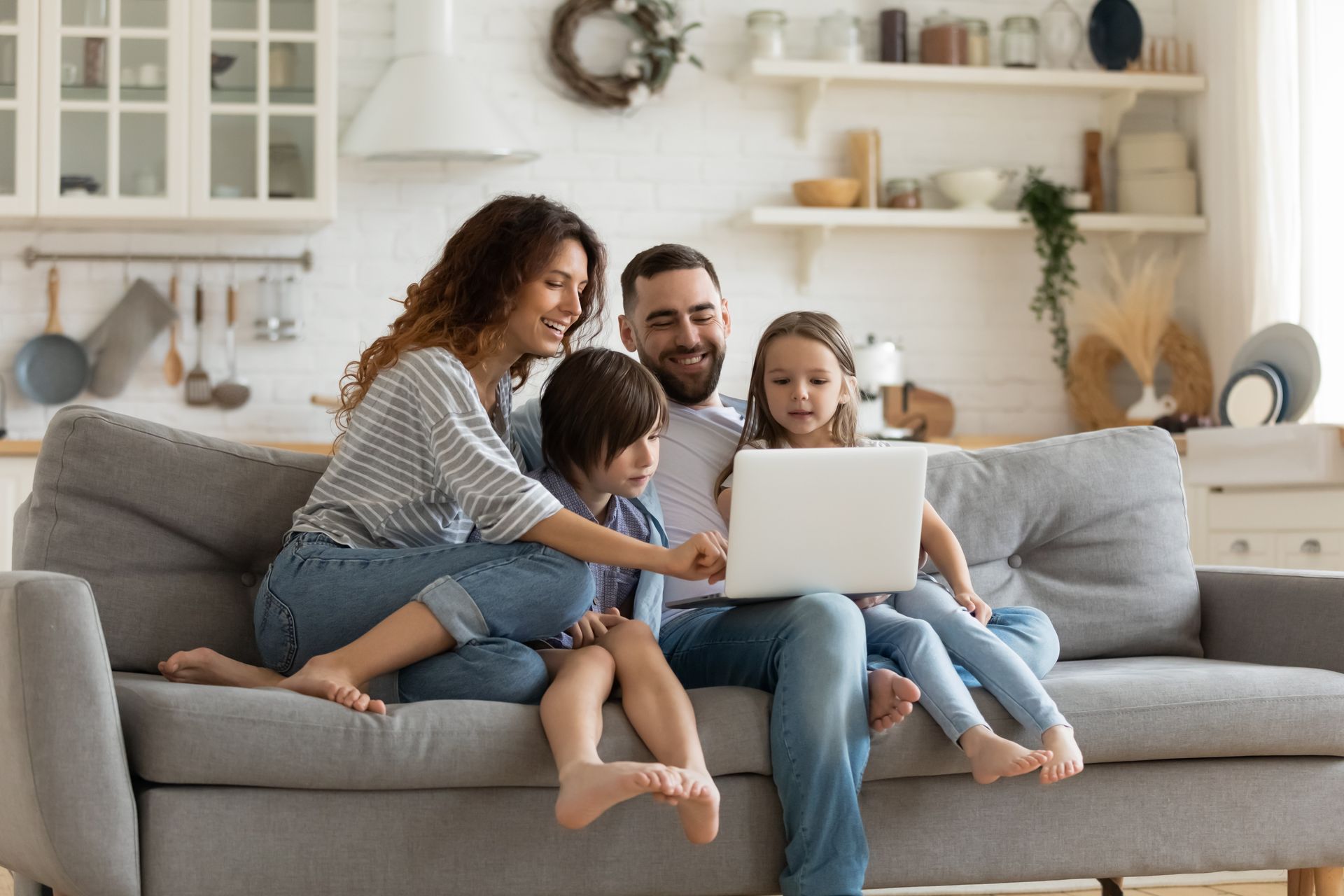 Une famille assise sur un canapé, réunie autour d'un ordinateur portable dans un salon lumineux.