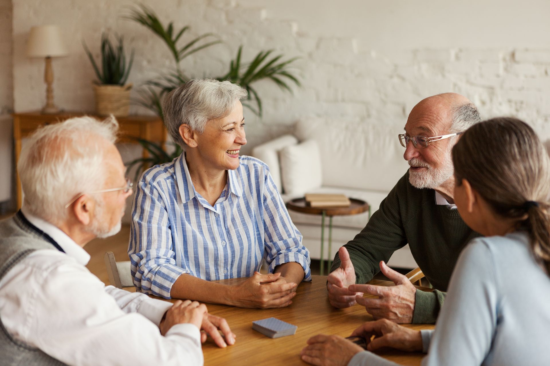 Quatre personnes discutent autour d'une table en bois dans un salon lumineux.