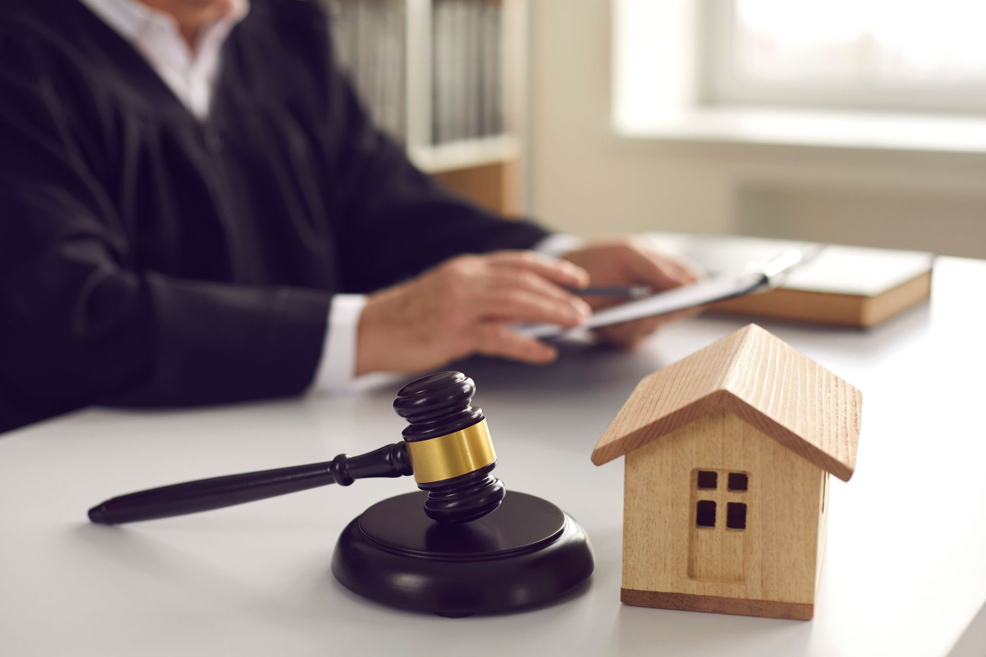 Un avocat, assis à son bureau avec un marteau et une maquette de maison, discute de documents sur un ordinateur portable.