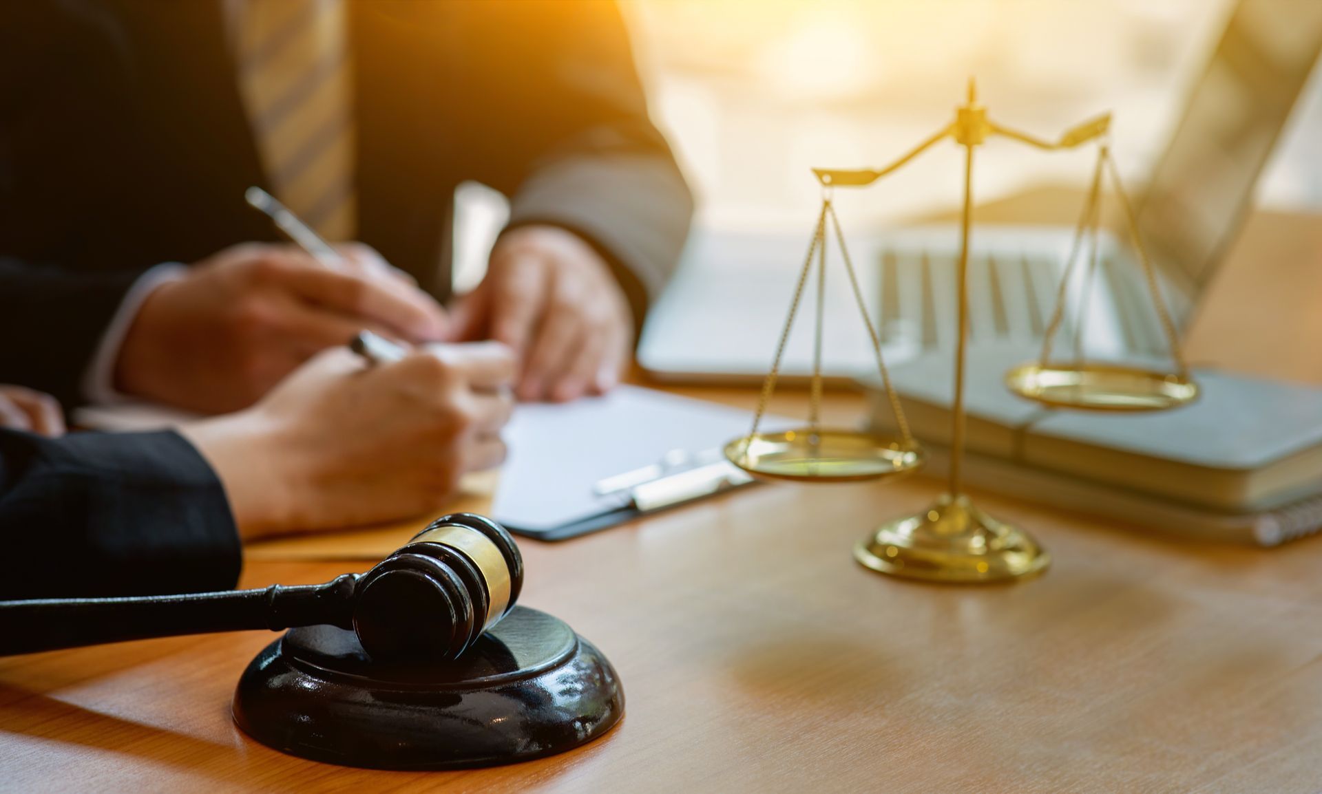 Un avocat prend des notes à côté d'un maillet et d'une balance de la Justice sur un bureau.
