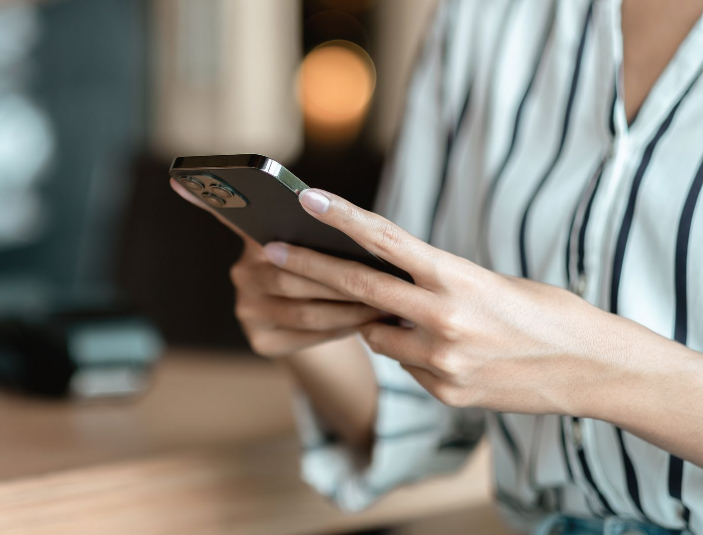 Une personne portant une chemise à rayures utilise un smartphone.