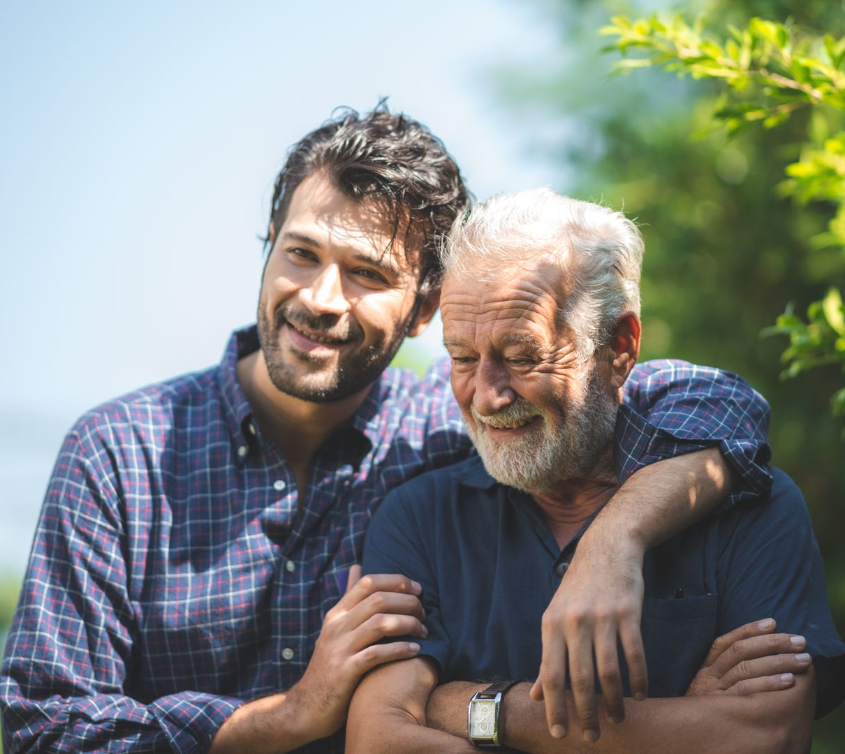 Deux hommes souriants se tiennent côte à côte à l'extérieur, l'un avec un bras autour de l'autre.