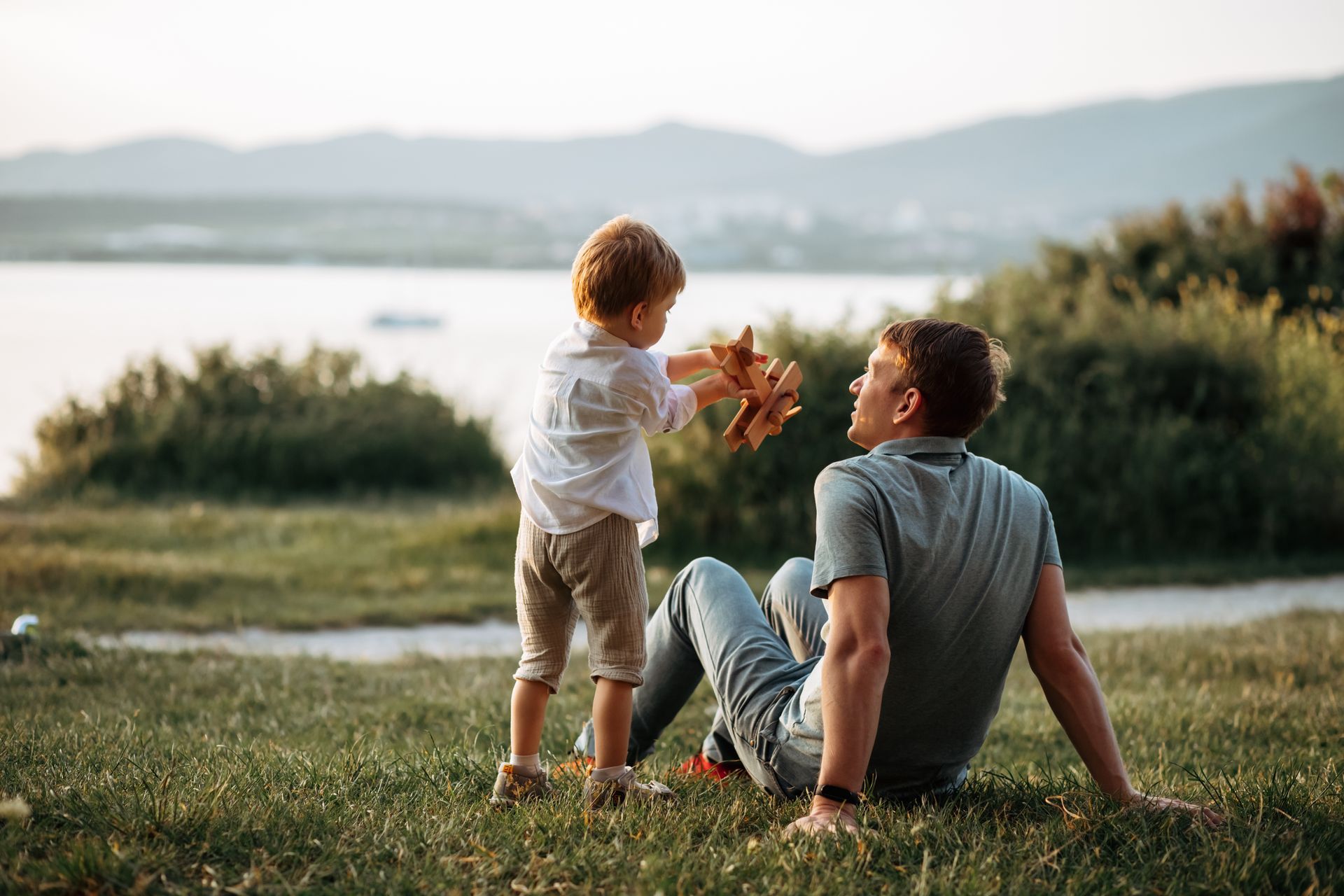 Un adulte et un enfant assis dans l'herbe au bord d'un lac.