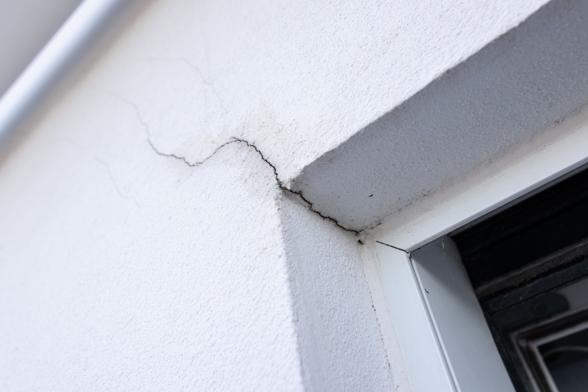 Fissure capillaire dans un mur extérieur près d'un cadre de fenêtre.