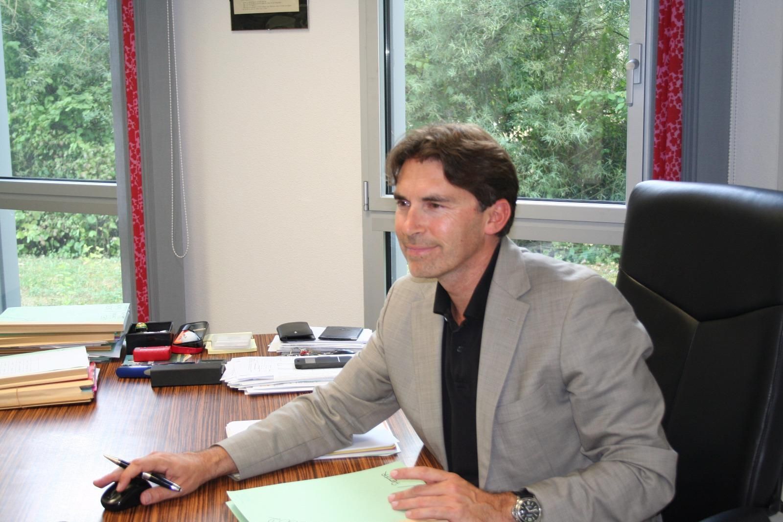 Maître Jean-Louis Colomb assis à son bureau près de grandes fenêtres.