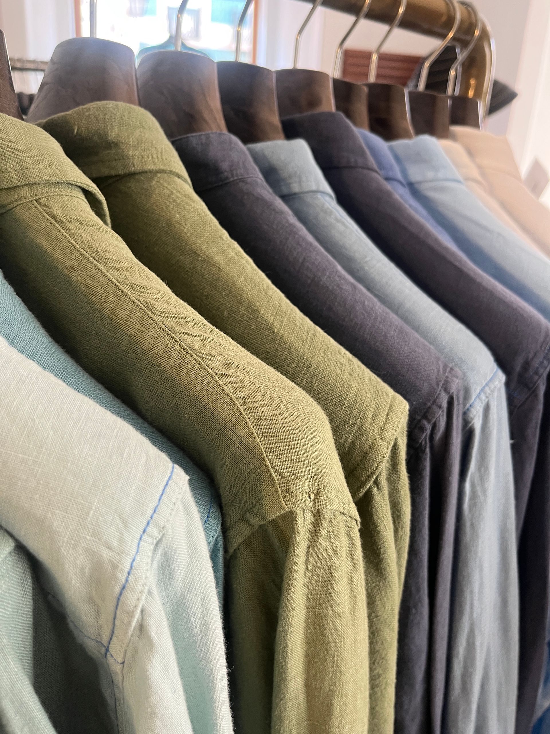 Camisas en tonos verdes y azules colgadas en un perchero.