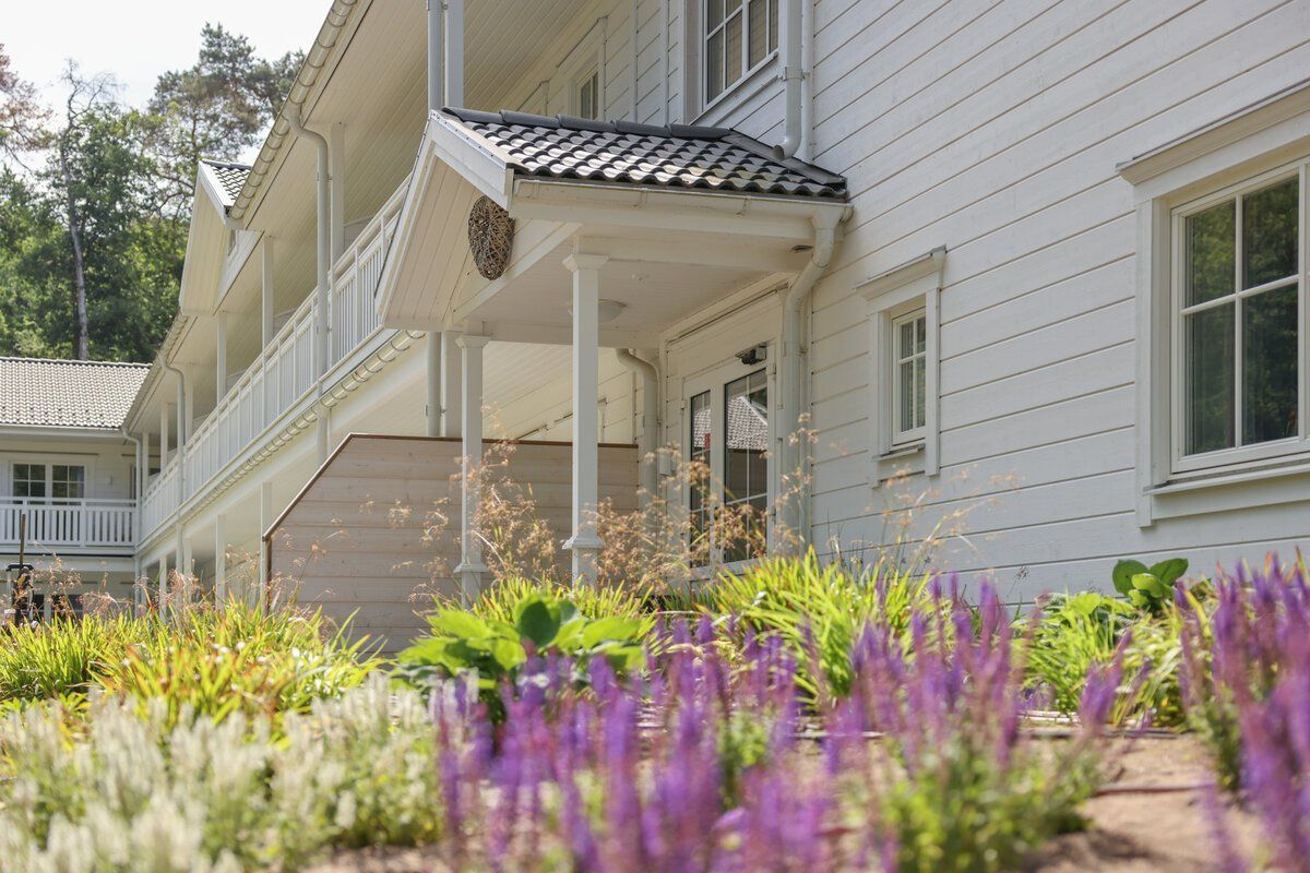 Ein weißes Haus mit lila Blumen davor.