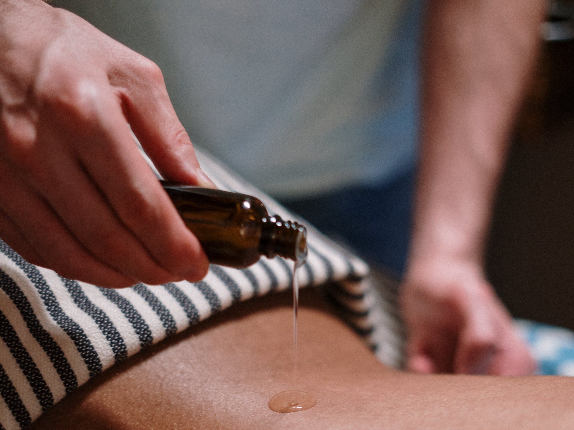 Eine Person bekommt eine Massage mit einer Flasche Öl auf dem Rücken.