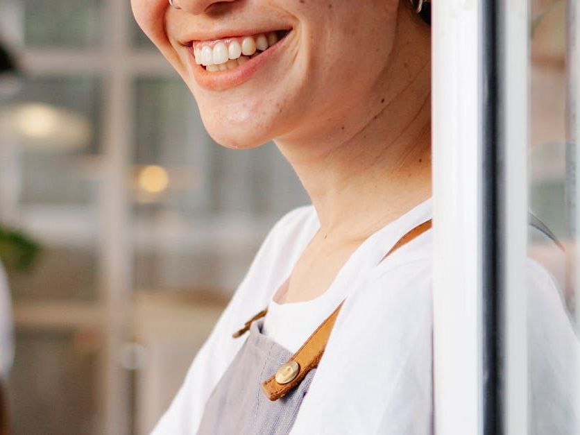 Eine Frau in einer Schürze steht lächelt vor einem Fenster.