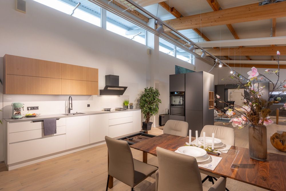 Moderne, offene Küche mit Essbereich, Holzdecke, weißen Schränken und einem langen Holztisch