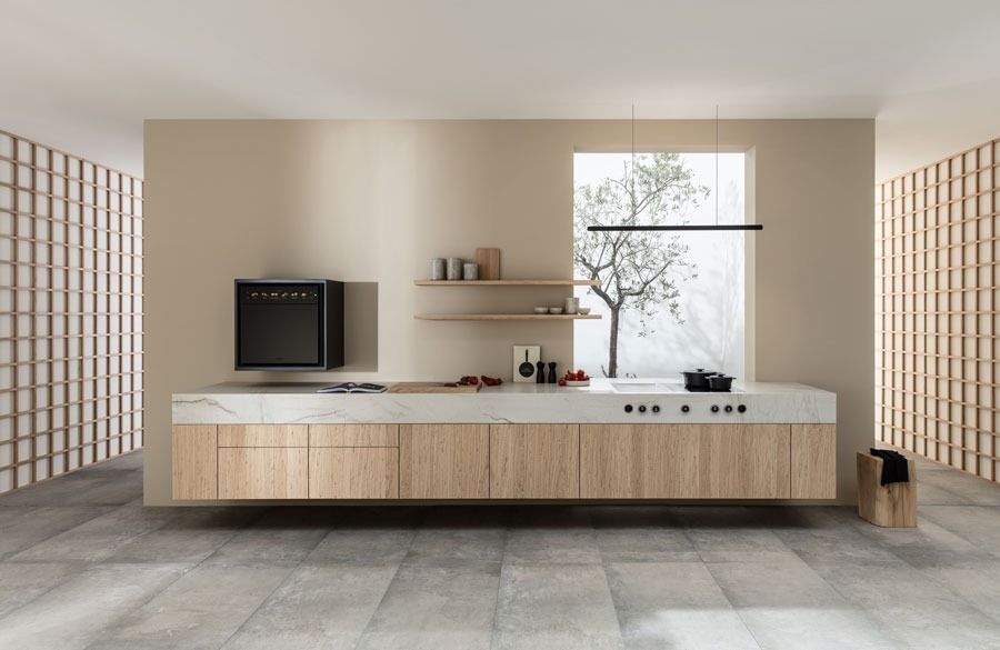 Minimalistische beige Küche mit Kochinsel, eingebautem Backofen, offenen Regalen und einem großen Fenster.