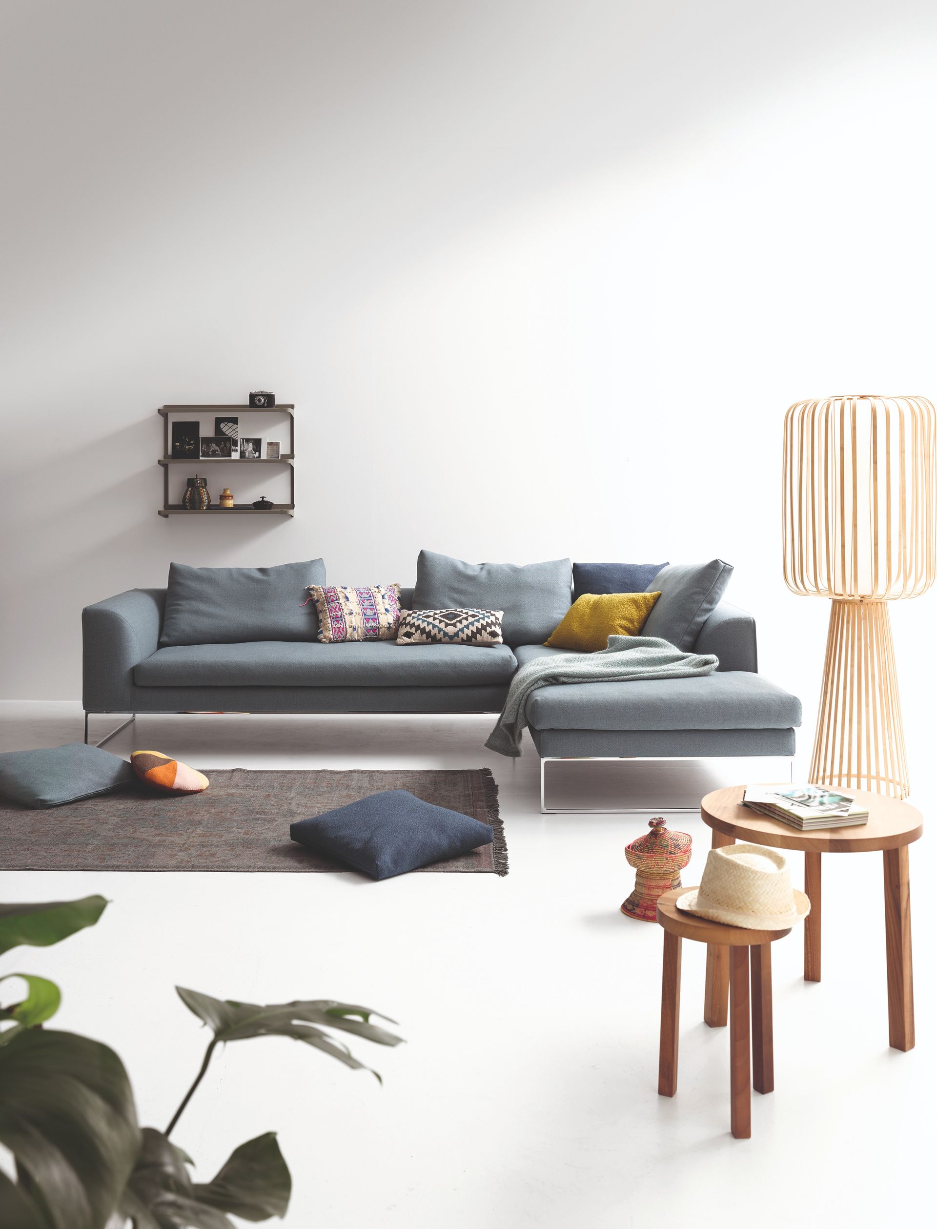Modernes Wohnzimmer mit grauem Ecksofa, Stehlampe, Teppich und Beistelltischen aus Holz.