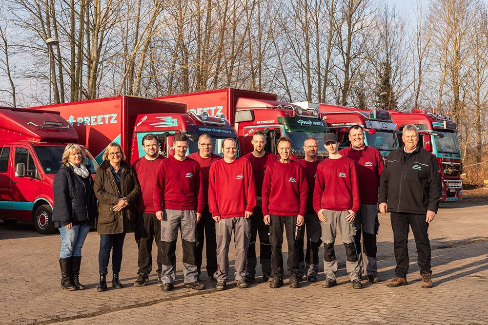 Eine Gruppe von Menschen posiert vor einer Reihe roter Lastwagen für ein Foto.