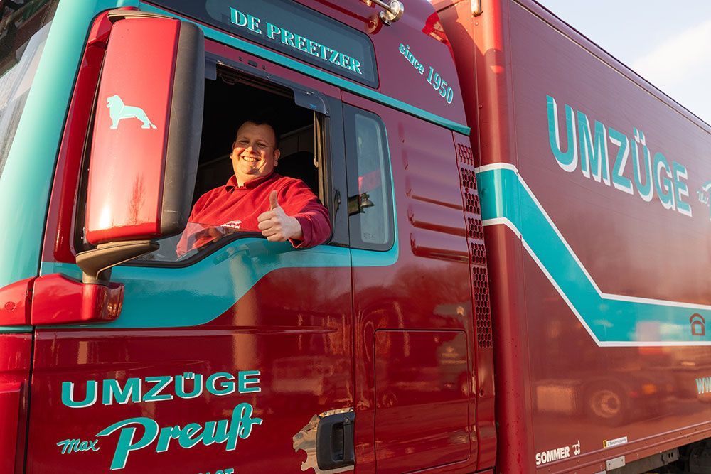 Ein Mann sitzt auf dem Fahrersitz eines roten Lastwagens und zeigt den Daumen nach oben.