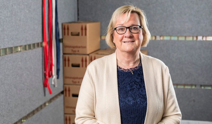 Eine Frau mit Brille steht vor einem Stapel Kartons.