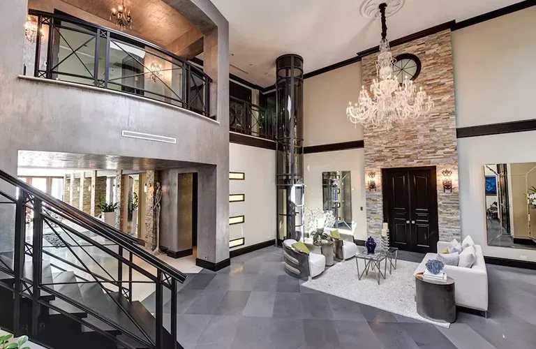 Intérieur luxueux avec grand escalier, ascenseur, lustre et coin salon moderne.