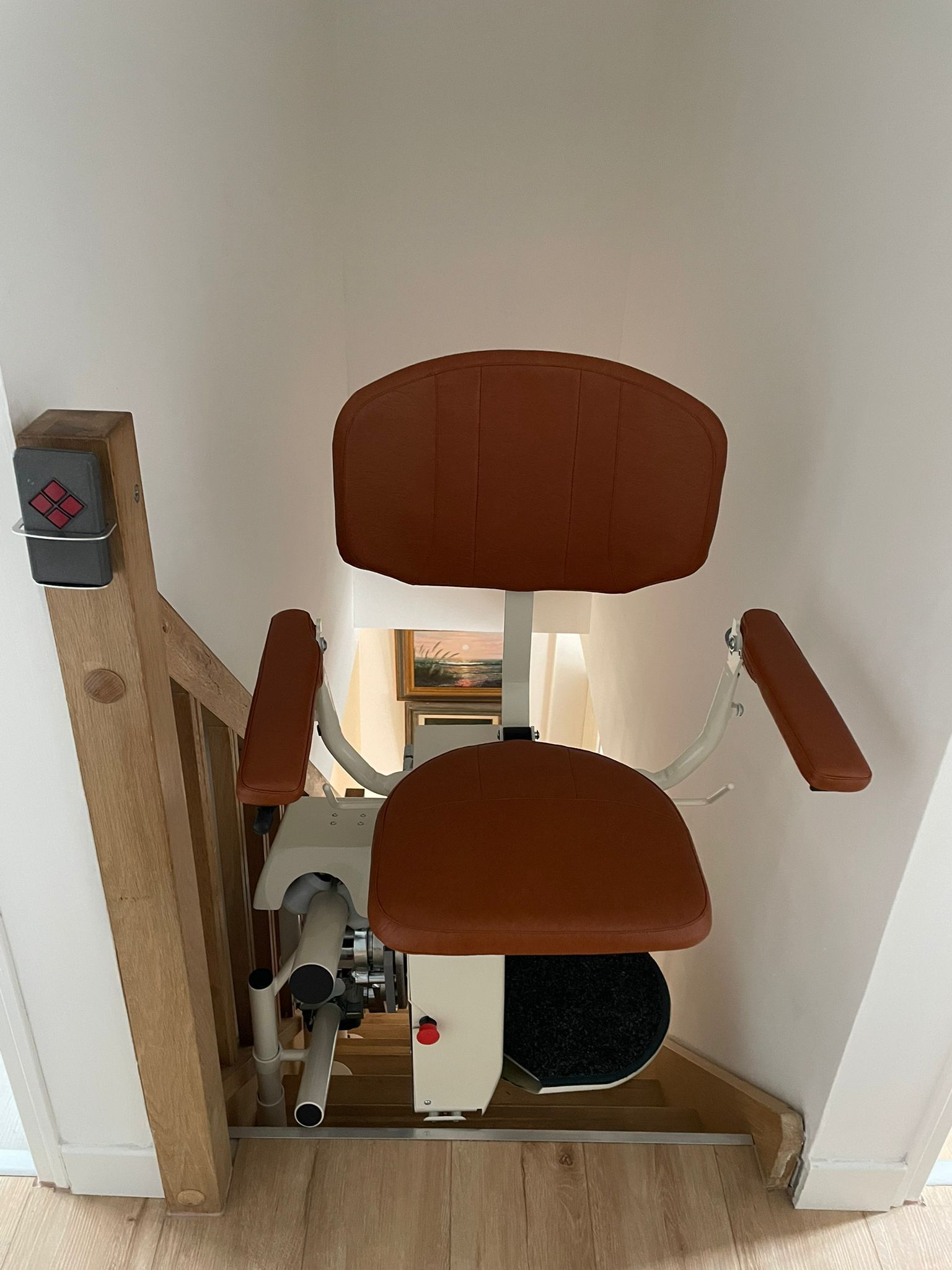 Fauteuil monte-escalier dans un couloir étroit à côté d'un escalier, avec siège et accoudoirs marron.