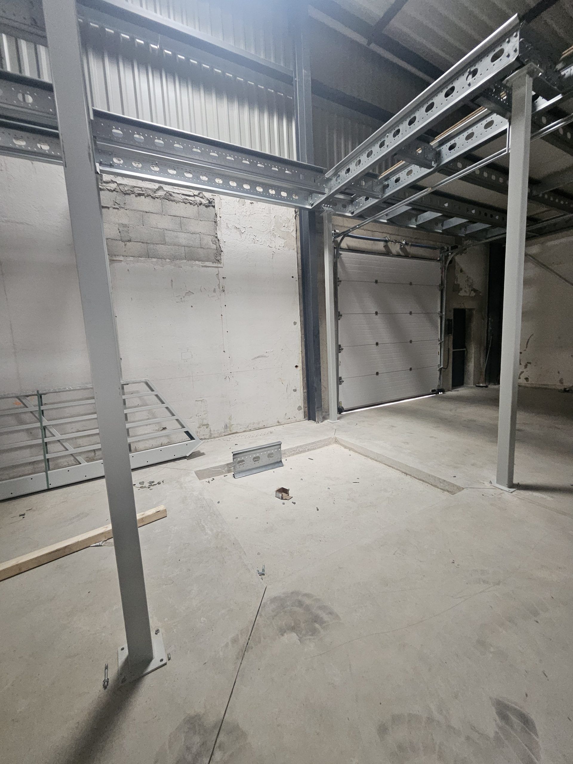 Pièce industrielle vide avec sol en béton, murs en briques blanches et structure de mezzanine en acier.