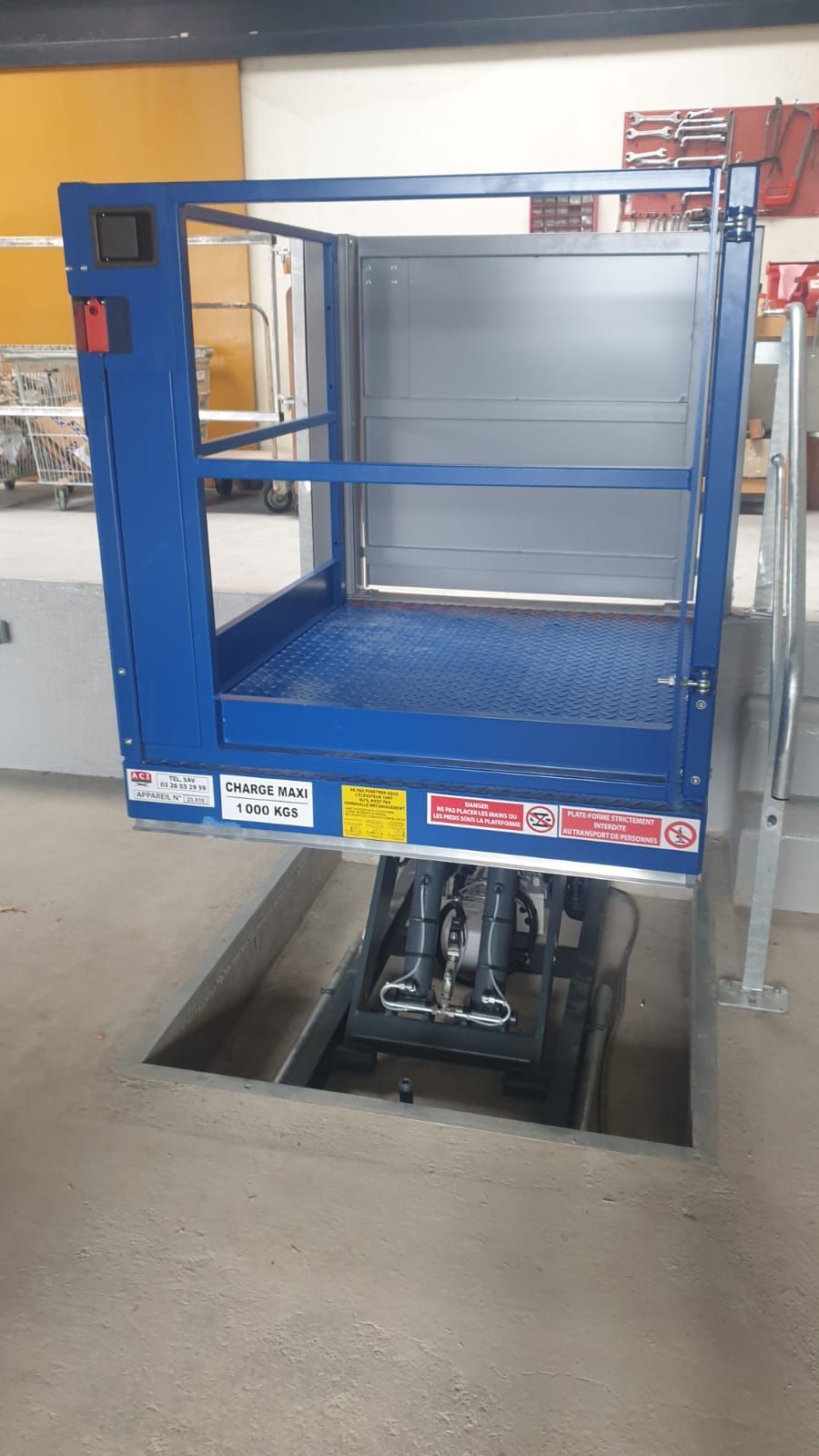 Plateforme élévatrice industrielle bleue à ciseaux au-dessus d'une fosse à ciel ouvert dans un atelier