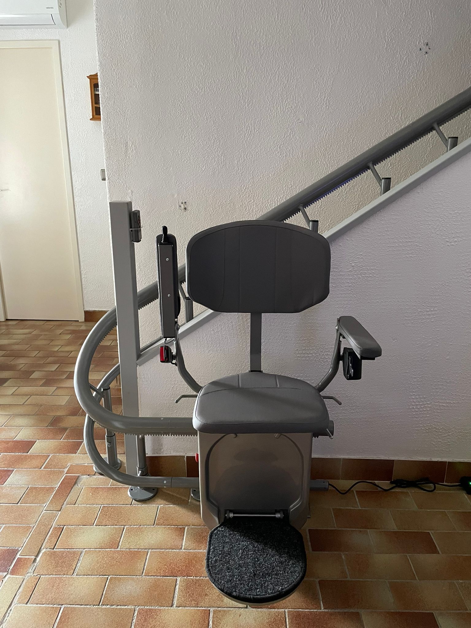Fauteuil monte-escalier avec siège et accoudoirs gris, sur un escalier adossé à un mur moucheté.